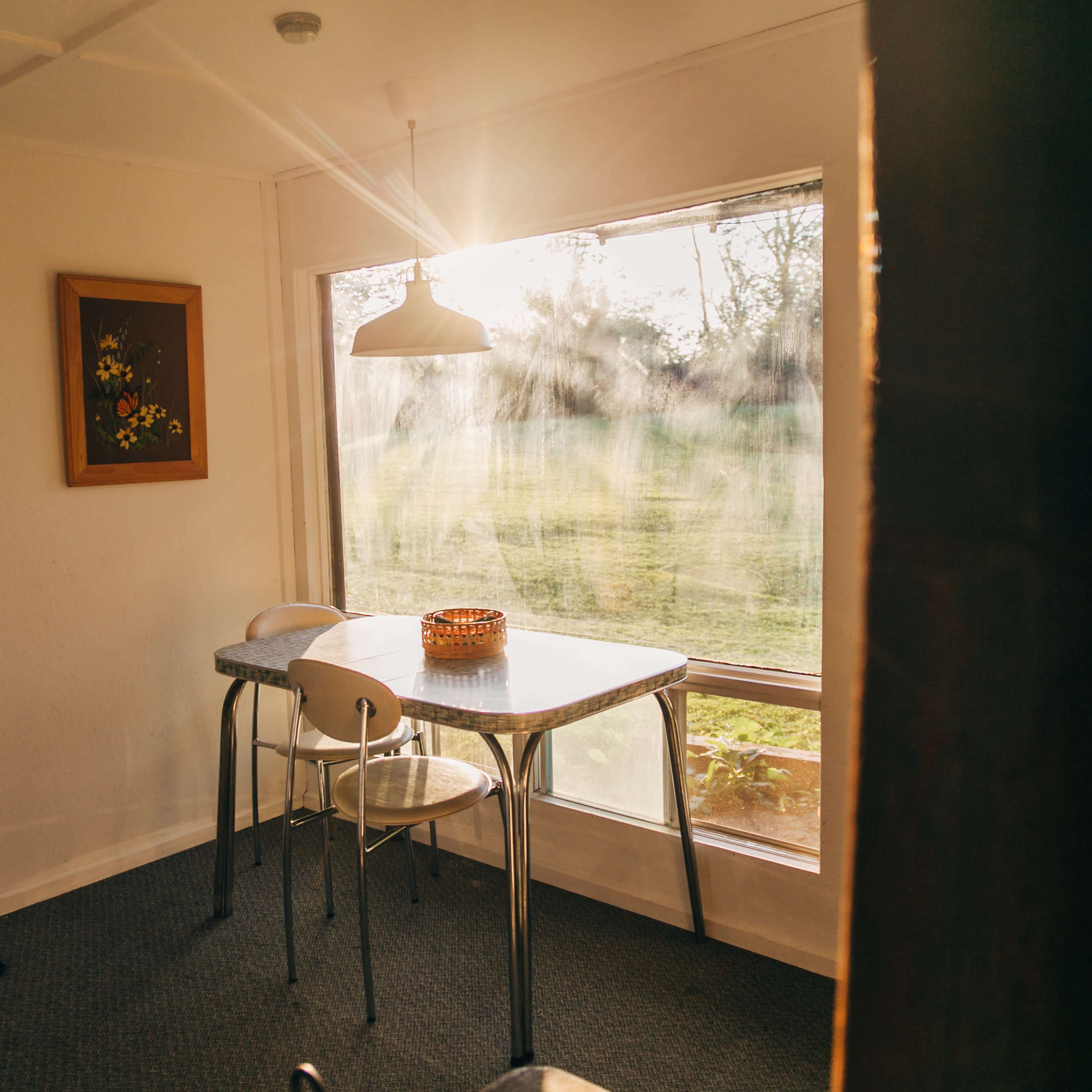 A small dining area features a table with two chairs beside a large window illuminated by sunlight.