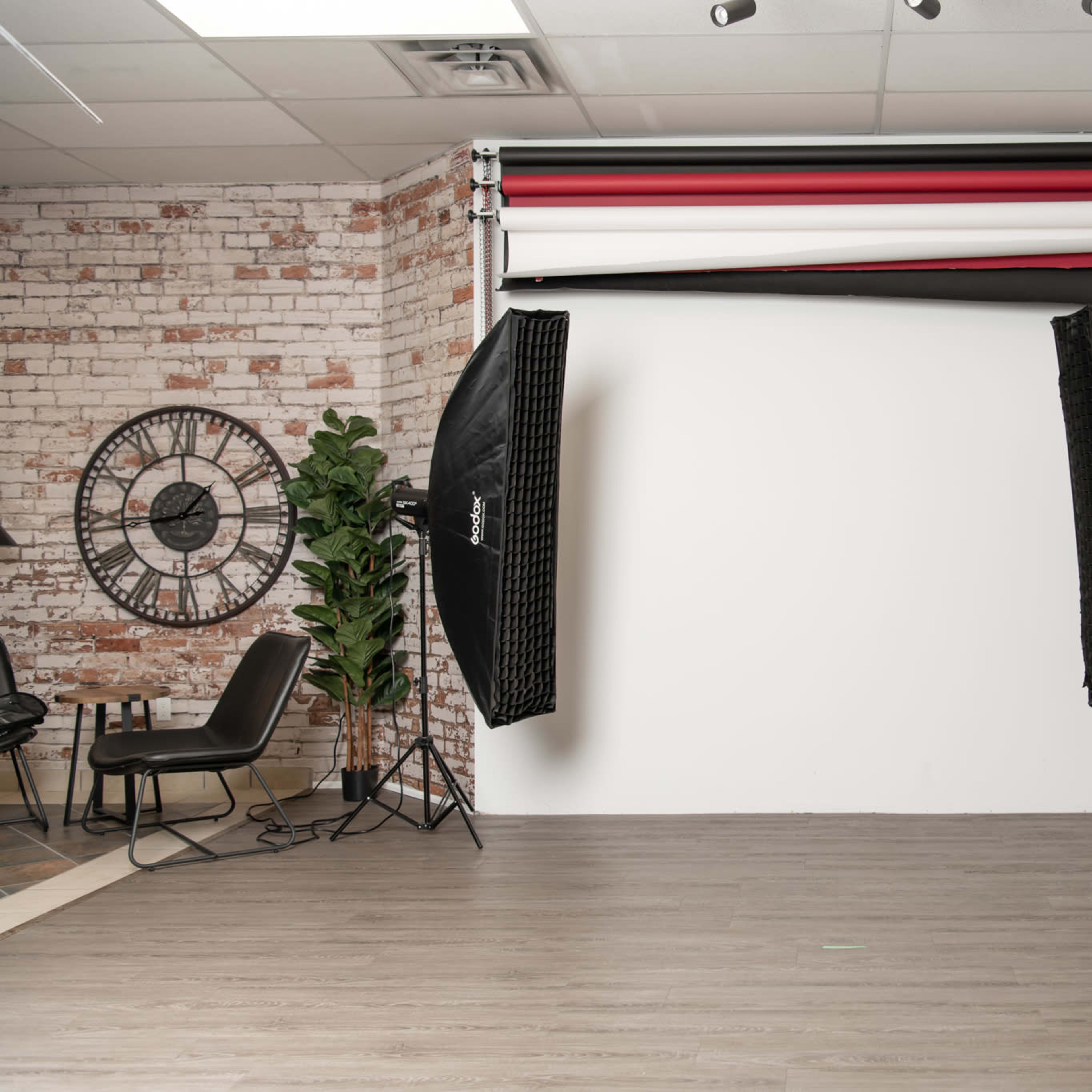 A photography studio featuring a white backdrop, two large softbox lights, a fan, and a few pieces of studio furniture.