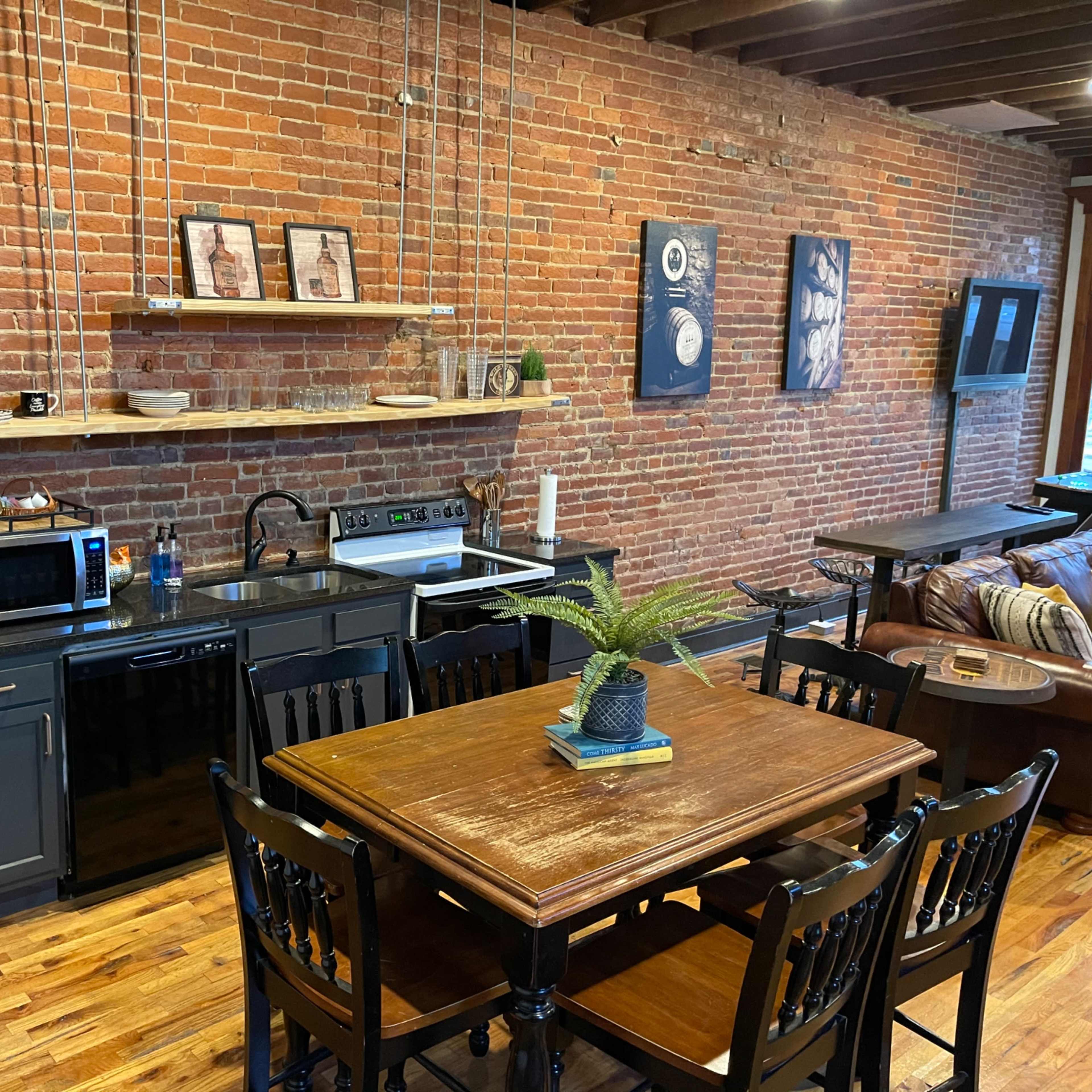 A kitchen area with exposed brick walls, a black refrigerator, dark cabinetry, and a wooden dining table set for four.