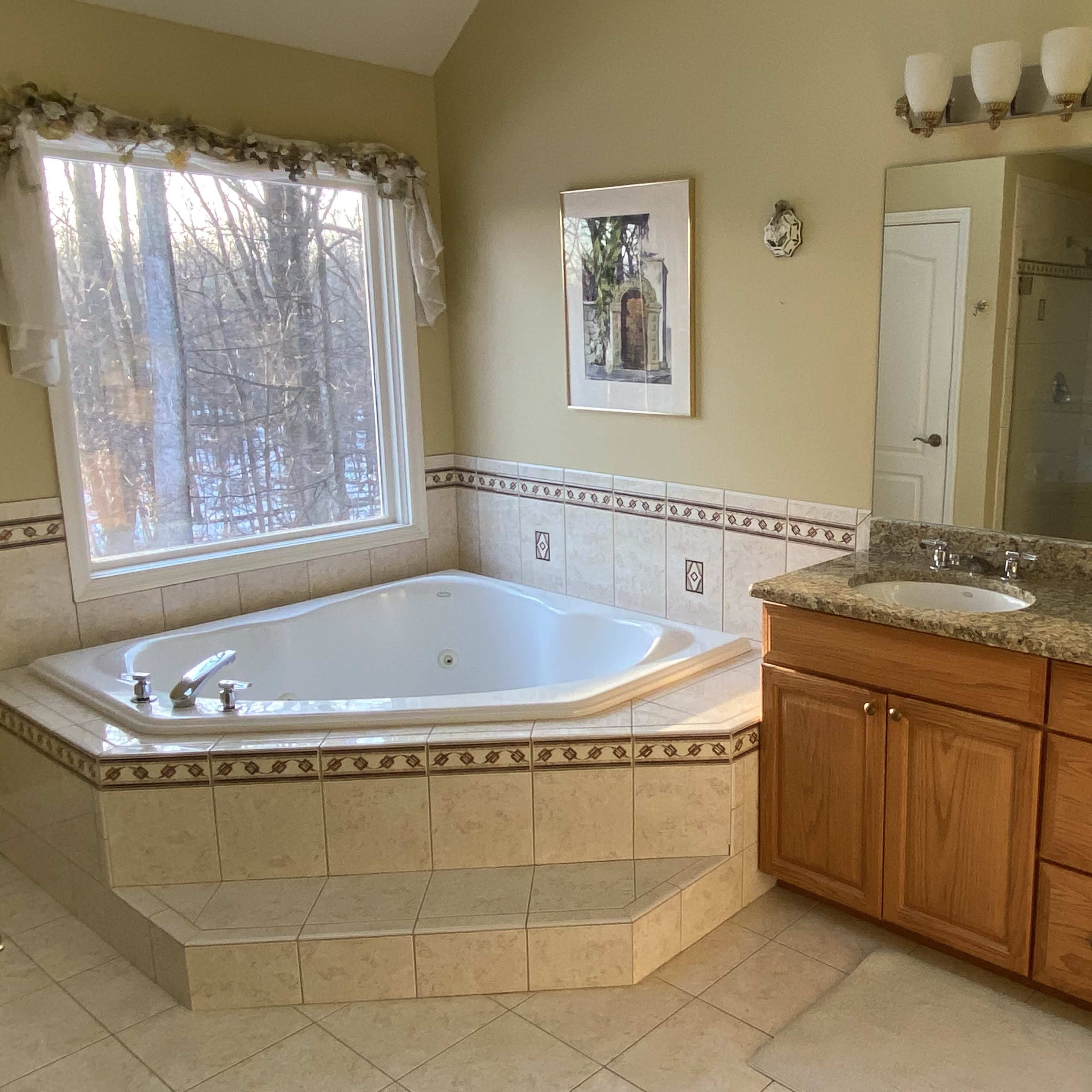 A bathroom with a jetted bathtub, dual sinks, and a large window overlooking a wooded area.