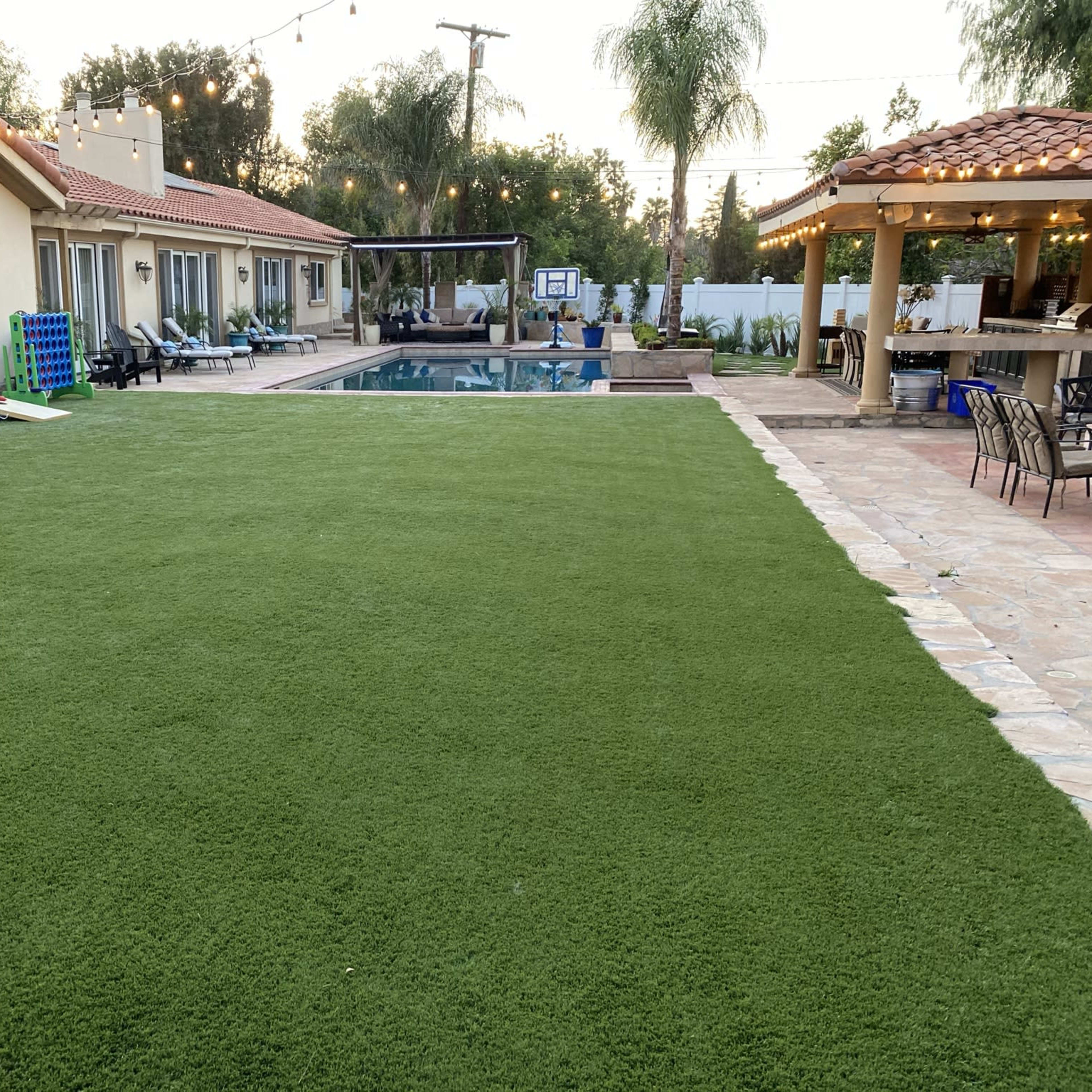 A backyard with a well-maintained green lawn, a swimming pool, and a patio area with string lights.