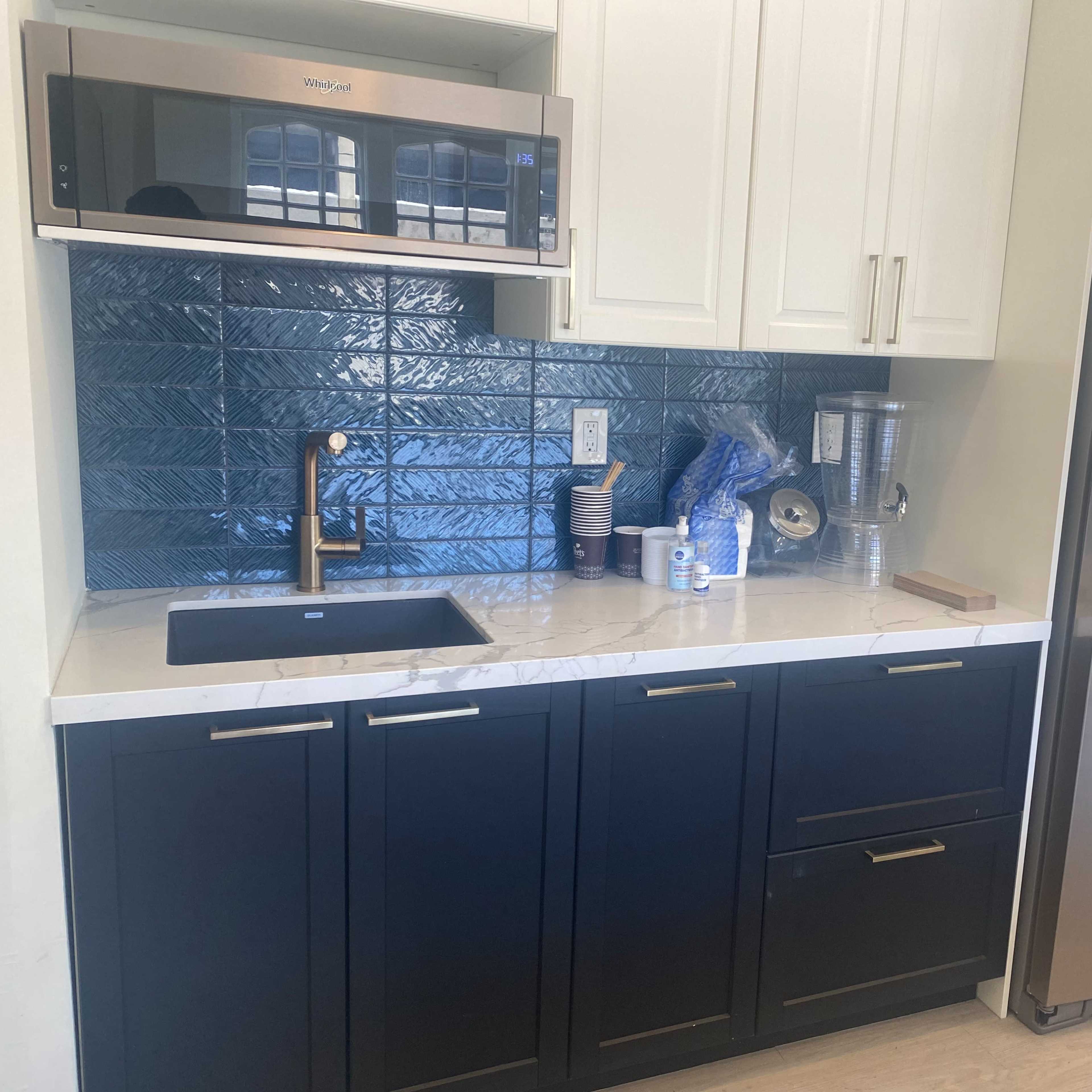 A modern kitchen with dark cabinetry, a stainless steel refrigerator, a microwave above the sink, and a blue tiled backsplash.