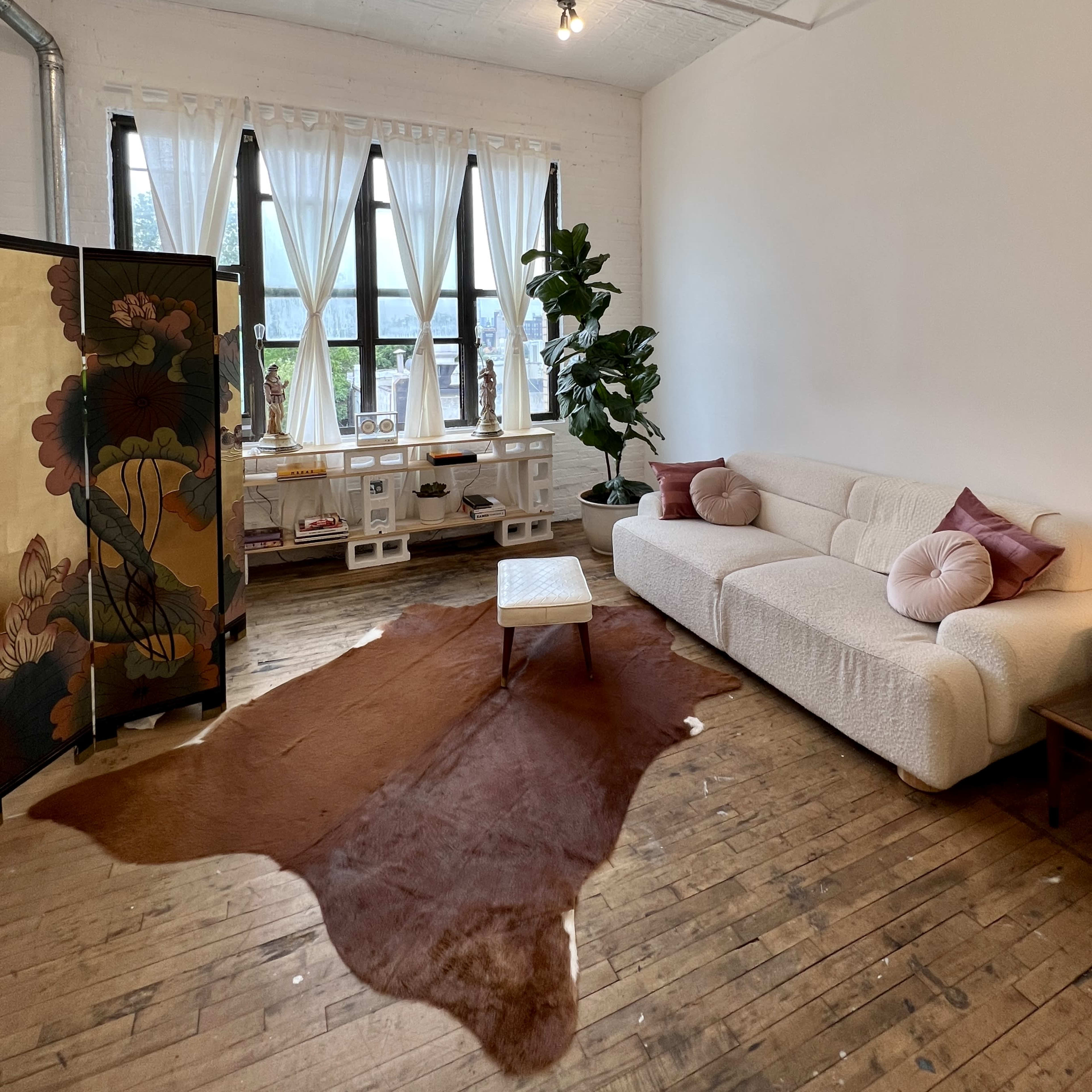 A bright living room with a white couch, a wooden coffee table, a decorative screen, and large windows letting in natural light.