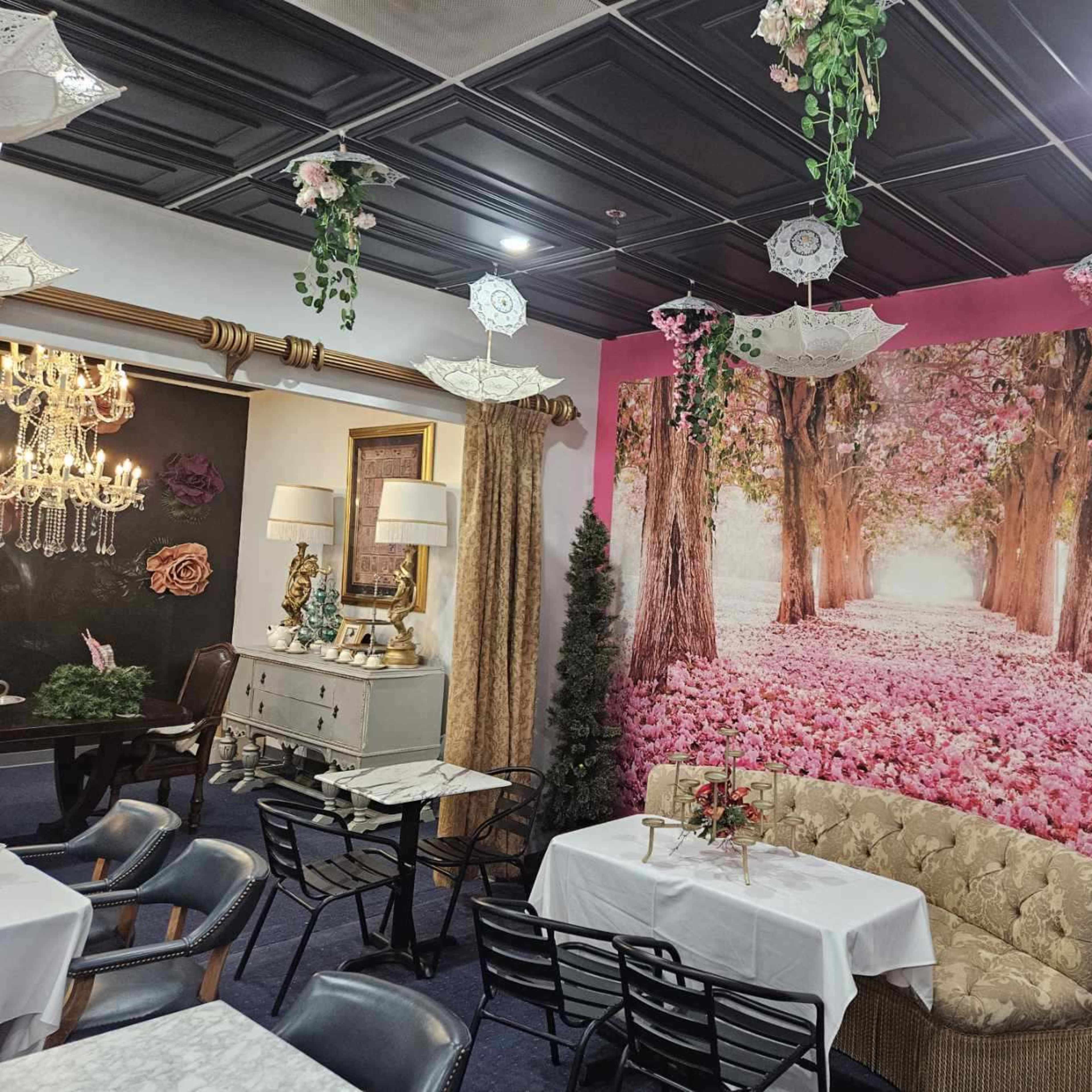 A restaurant interior featuring a mural of a tree-lined path with pink flowers, complemented by decorative umbrellas hanging from the ceiling.