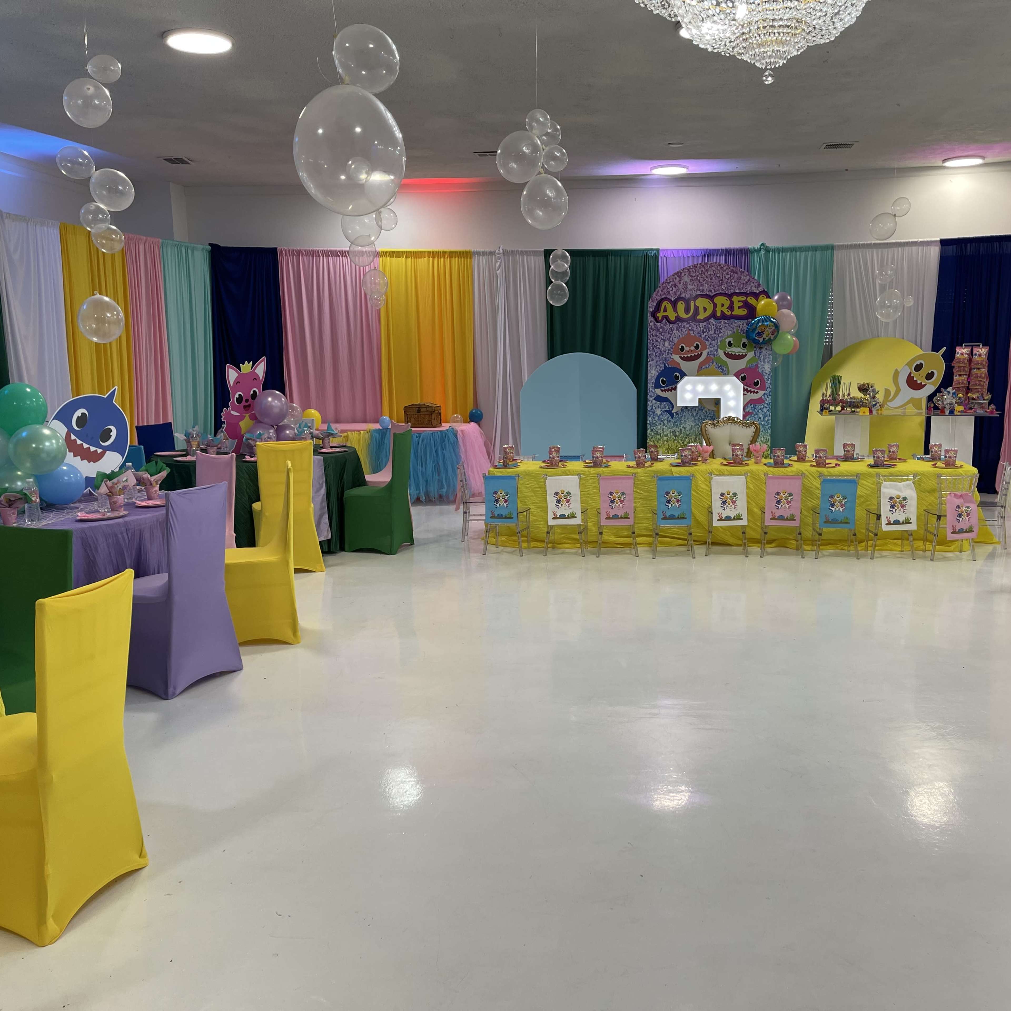 A brightly decorated party space features tables adorned with colorful tablecloths, balloons, and a themed display for an event named "Audrey's."
