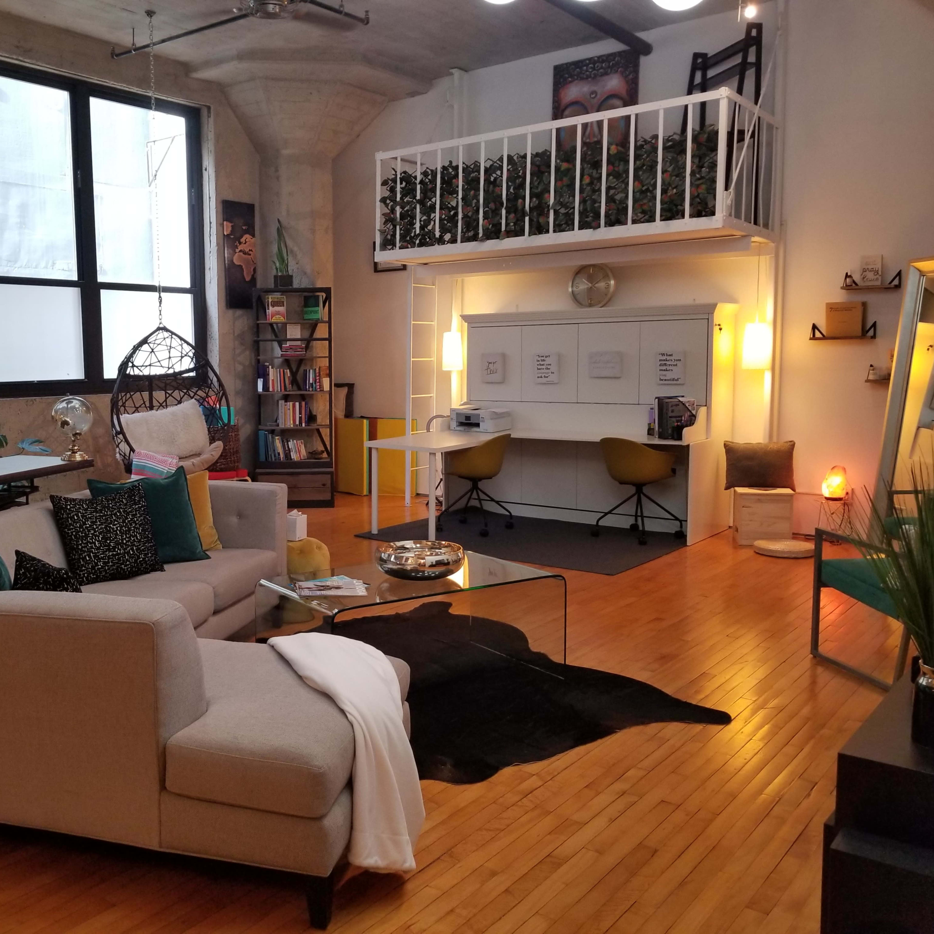 A modern open-concept living space with a sofa, a glass coffee table, a lofted bed area, and a workspace featuring two chairs and a round table.