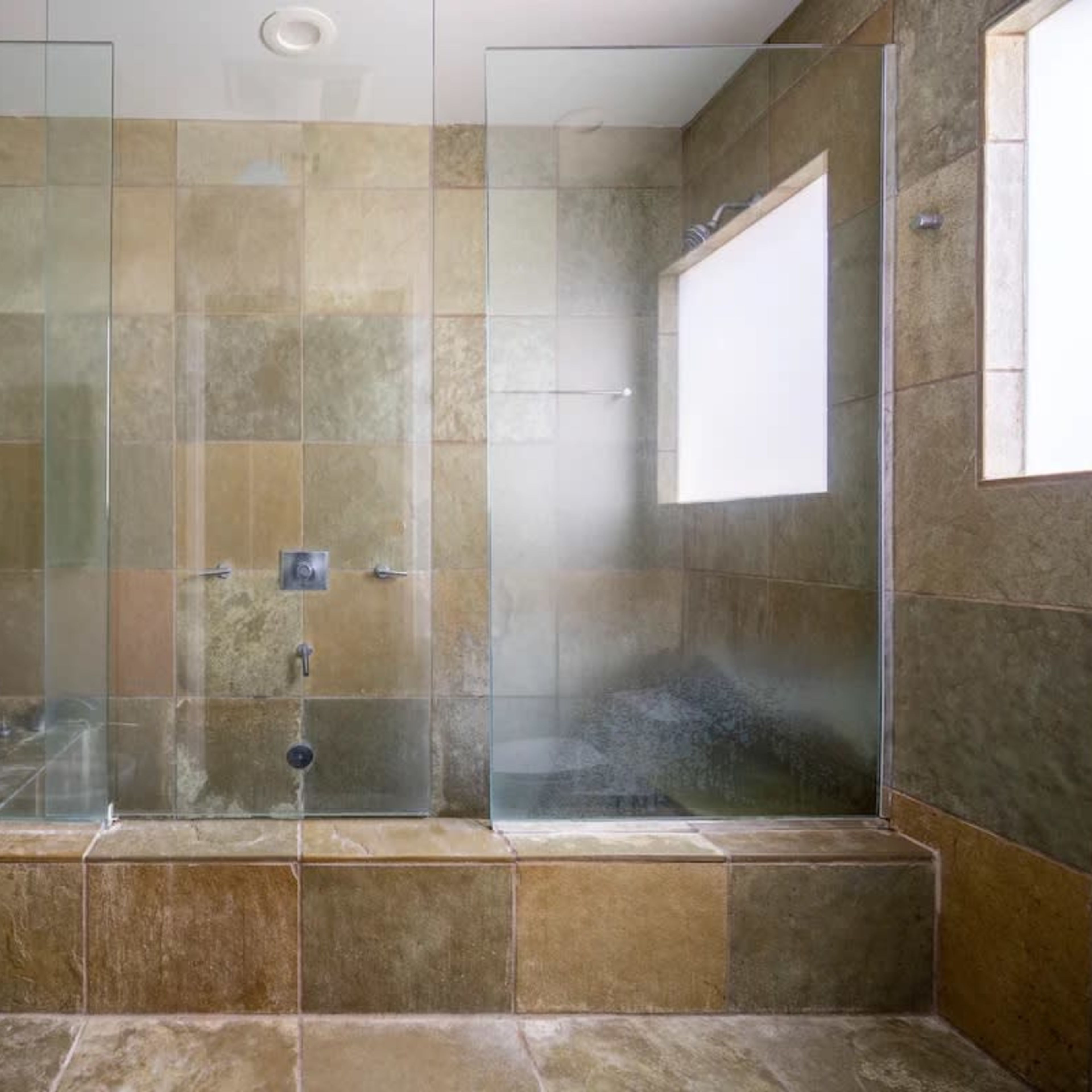 A modern bathroom featuring a spacious walk-in shower enclosed with glass panels and tiled in various shades of natural stone.