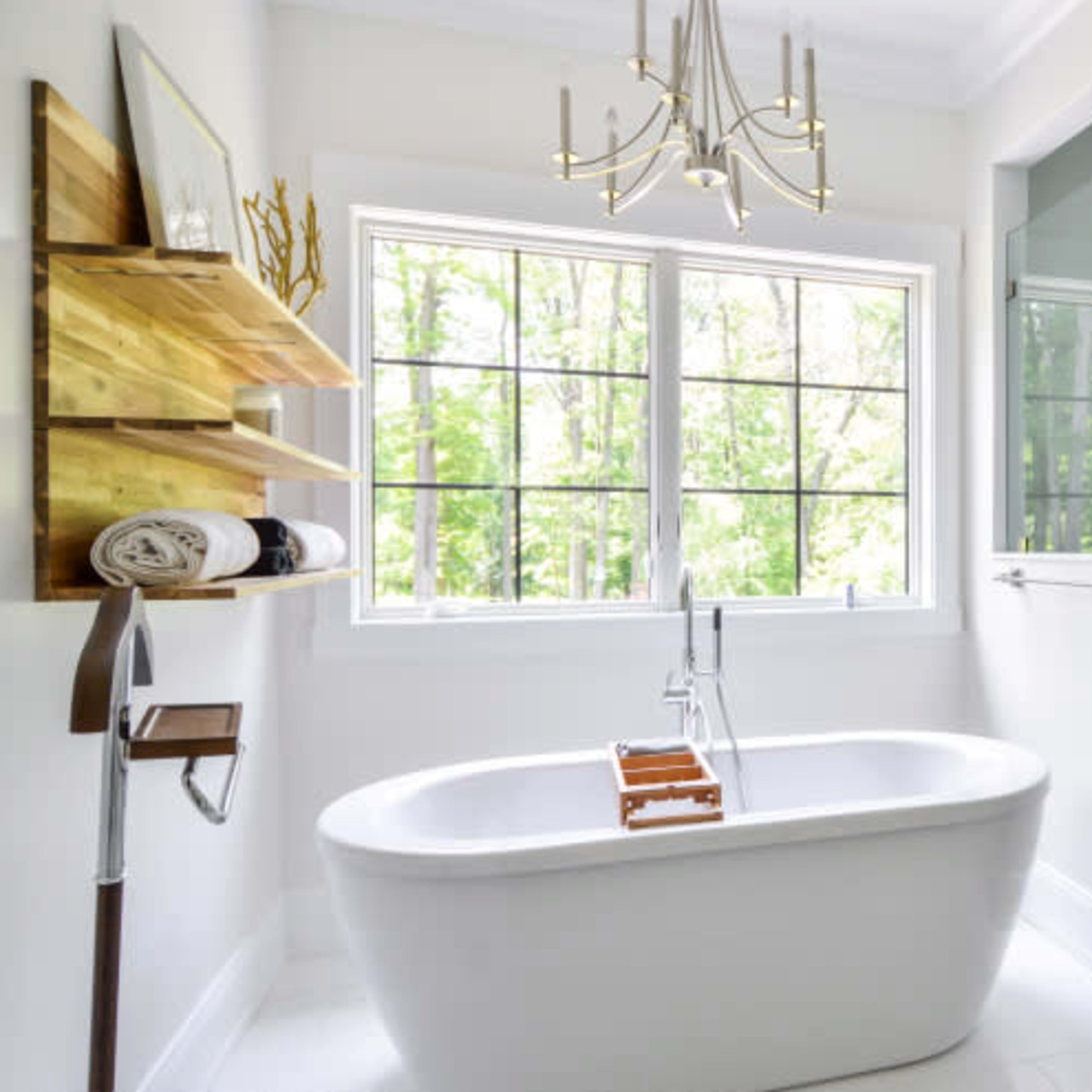A modern bathroom featuring a freestanding bathtub, a glass-enclosed shower, and a large window with a view of greenery.