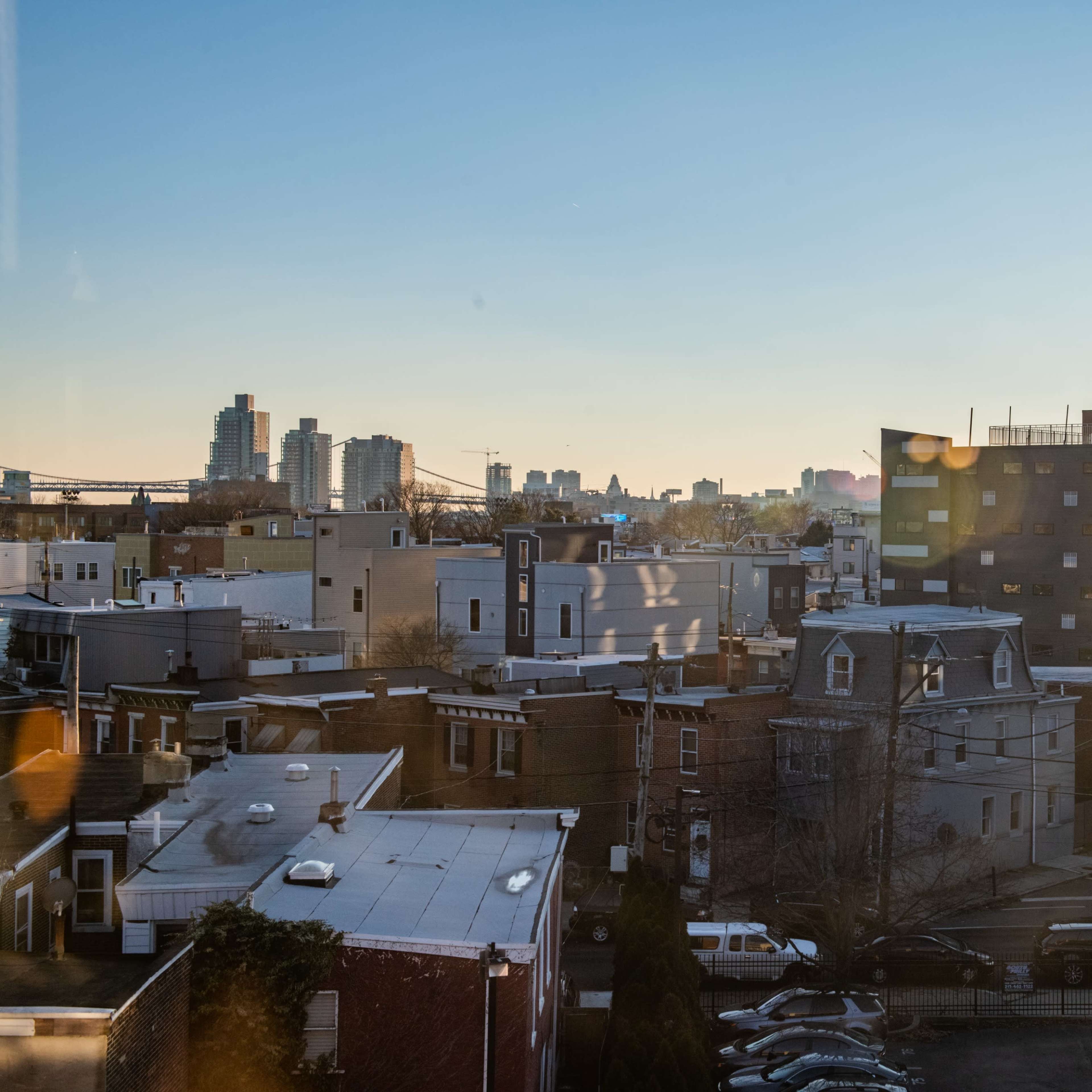 A city skyline at sunset, with buildings of varying heights and architectural styles visible in the foreground and background.