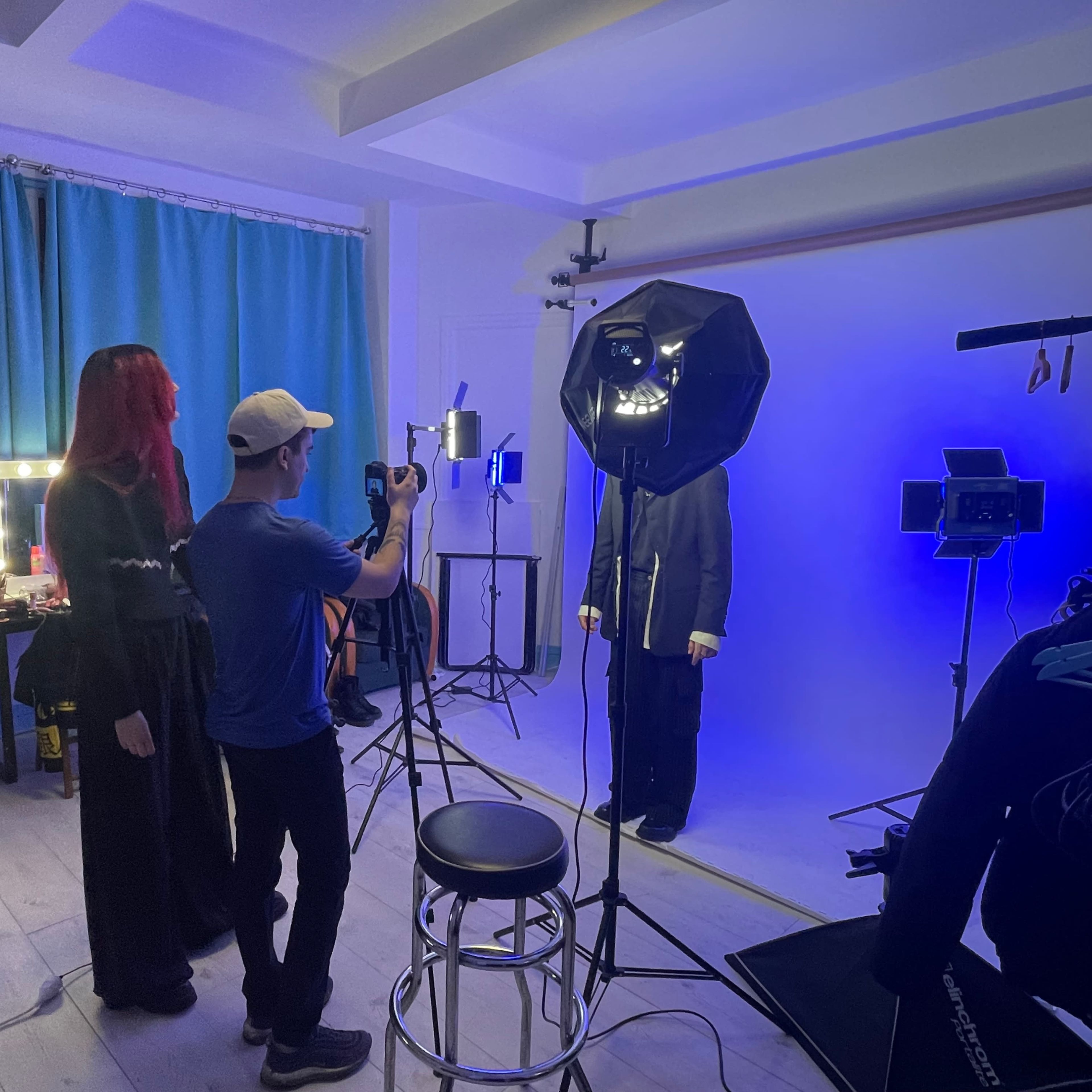 A photographer captures an individual posing against a blue backdrop in a studio while others work at computer desks.