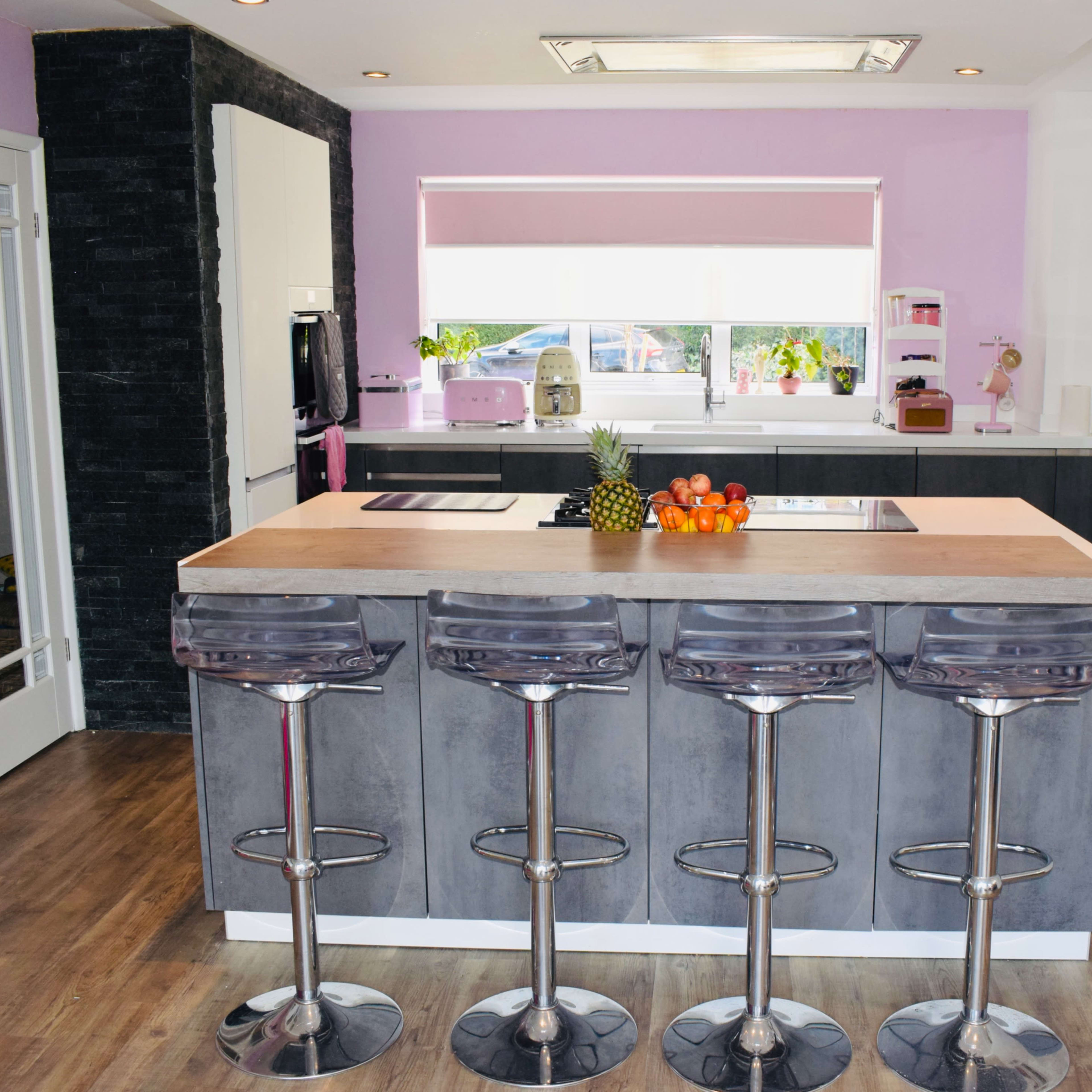 A modern kitchen features a central island with four bar stools, surrounded by light-colored cabinets and a large window letting in natural light.