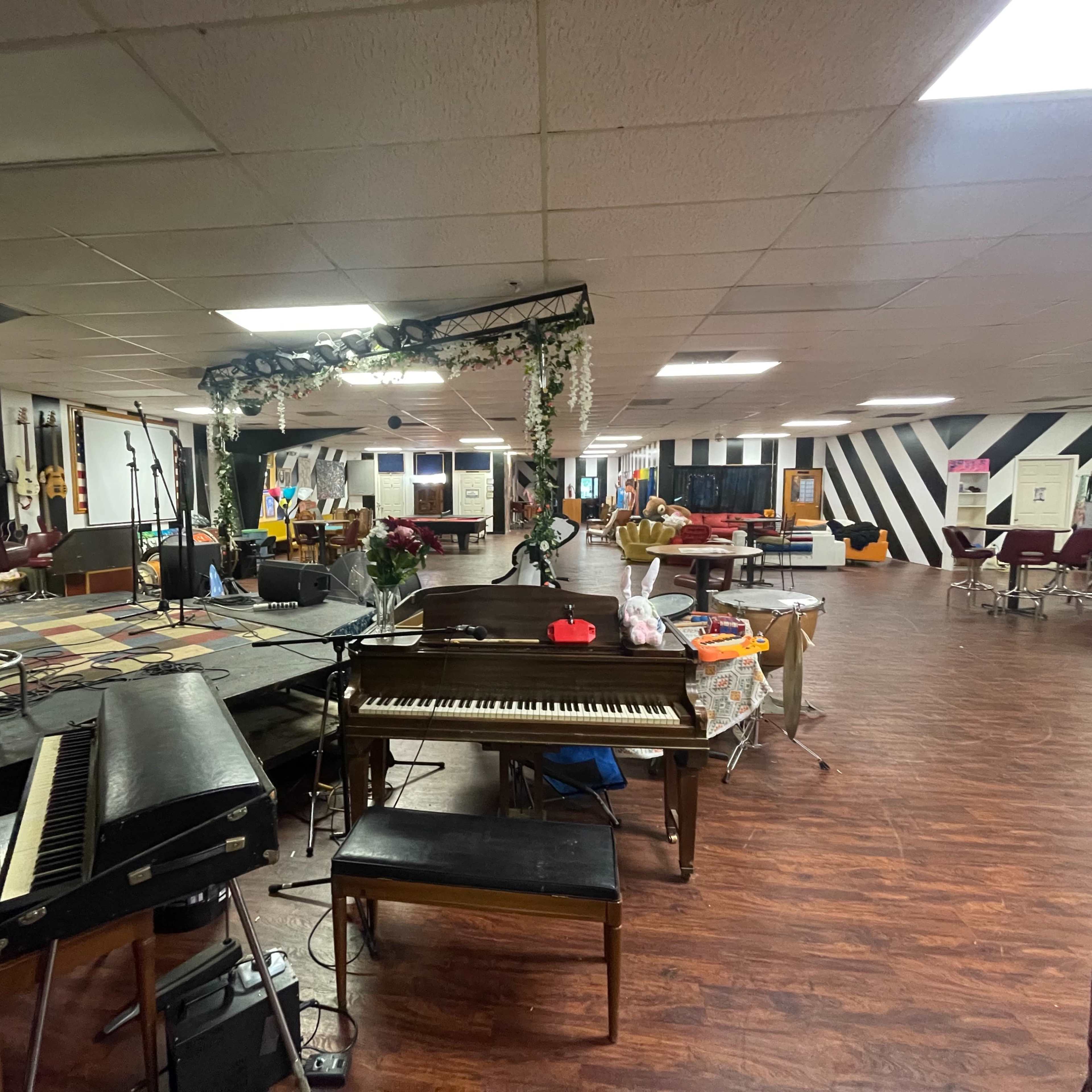 A spacious indoor venue with a stage set up for performances, featuring a piano and various seating arrangements.