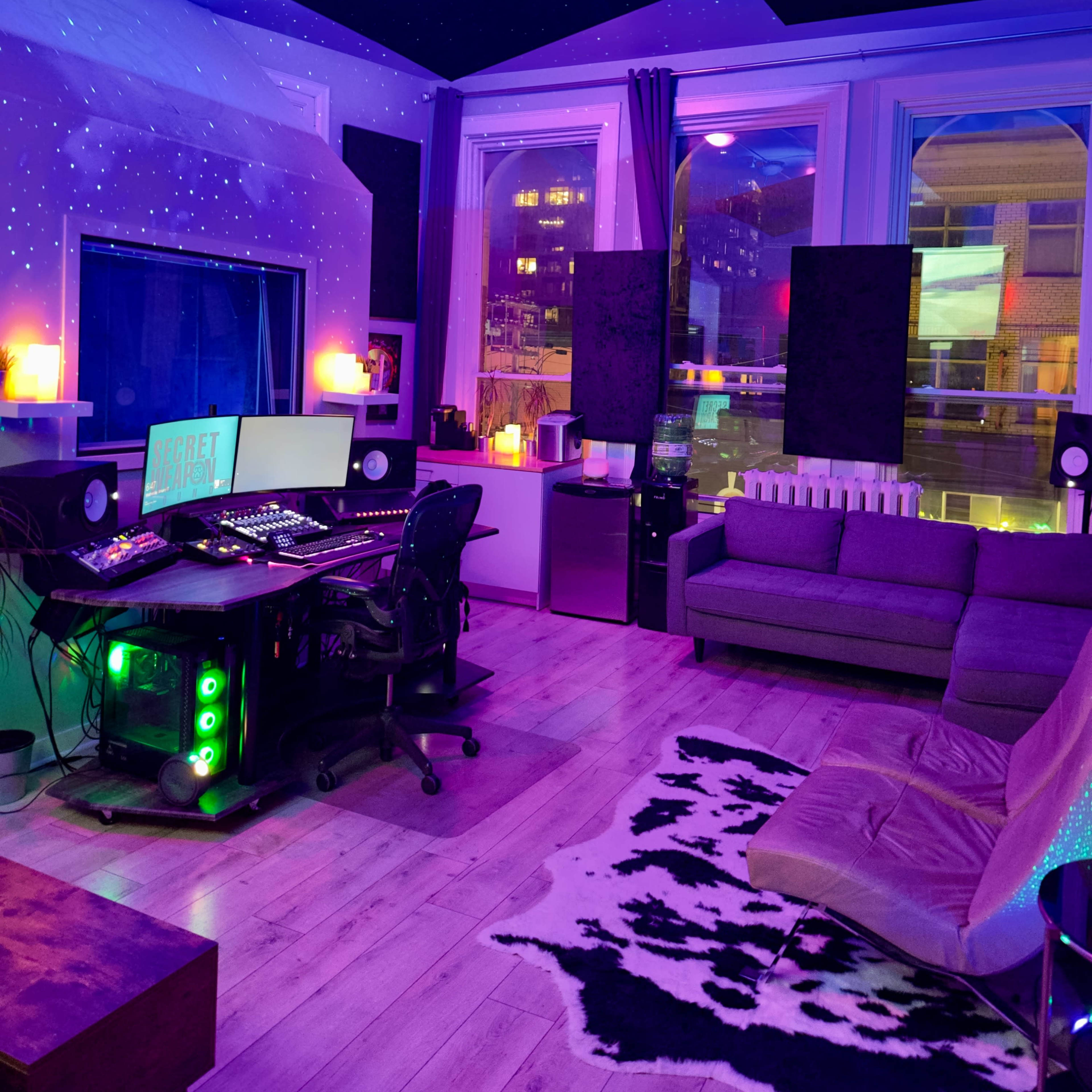 A modern studio space with a computer desk, a couch, and ambient lighting, featuring a projected starry ceiling and sound panels on the walls.