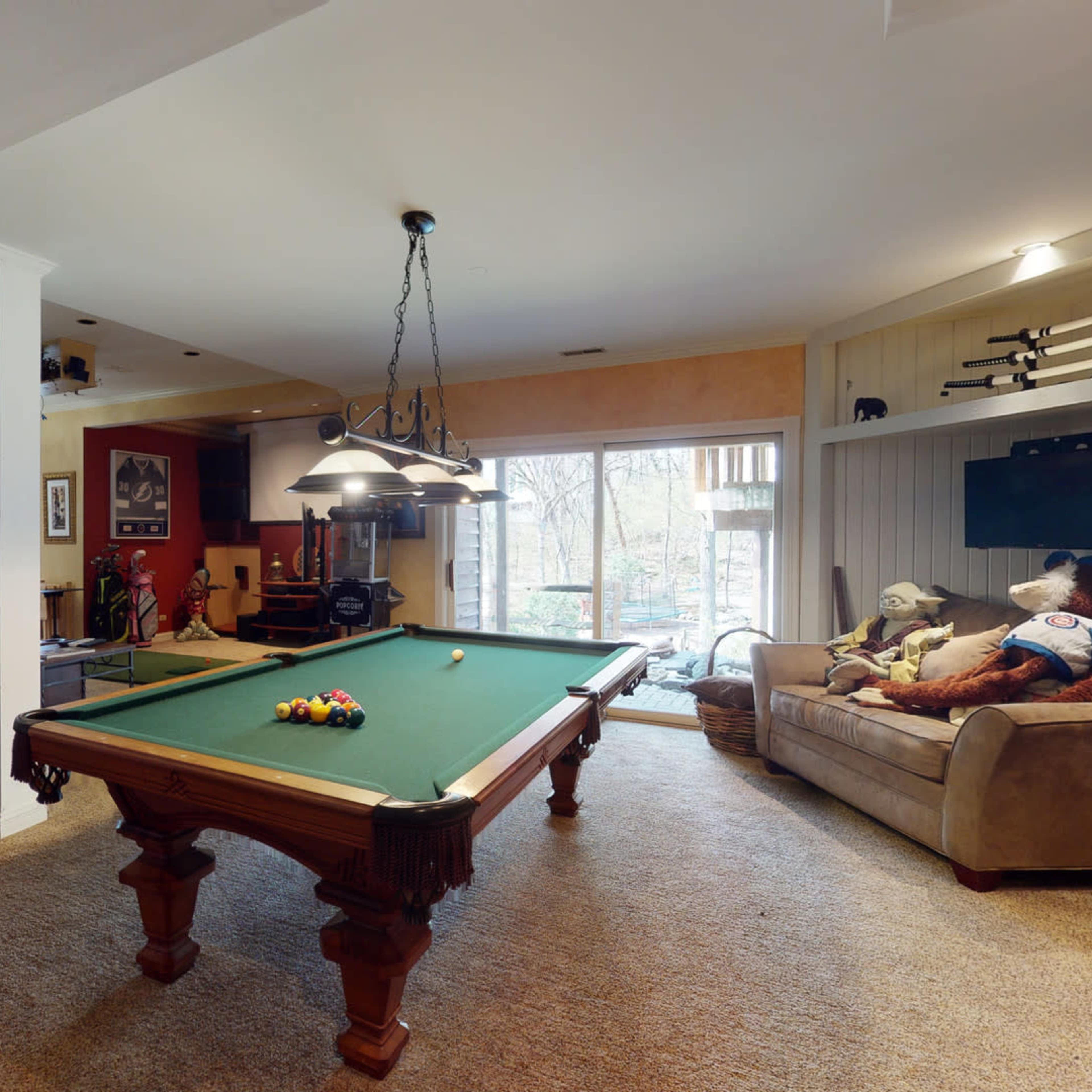 A spacious basement game room featuring a pool table, a foosball table, and a cozy seating area with a couch and stuffed animals.