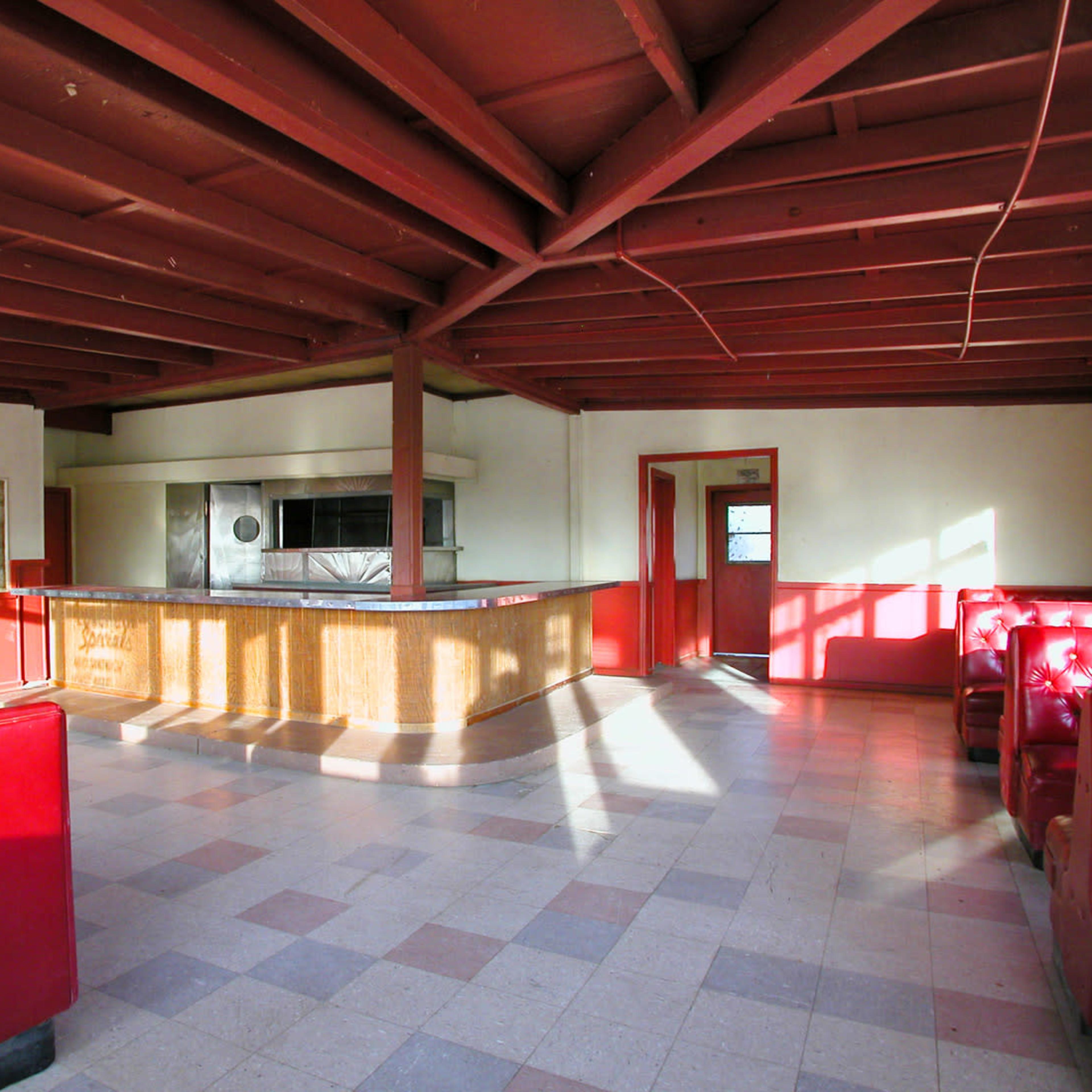 An empty room with red furniture and wooden beams, featuring a bar counter and a kitchen area in the background.