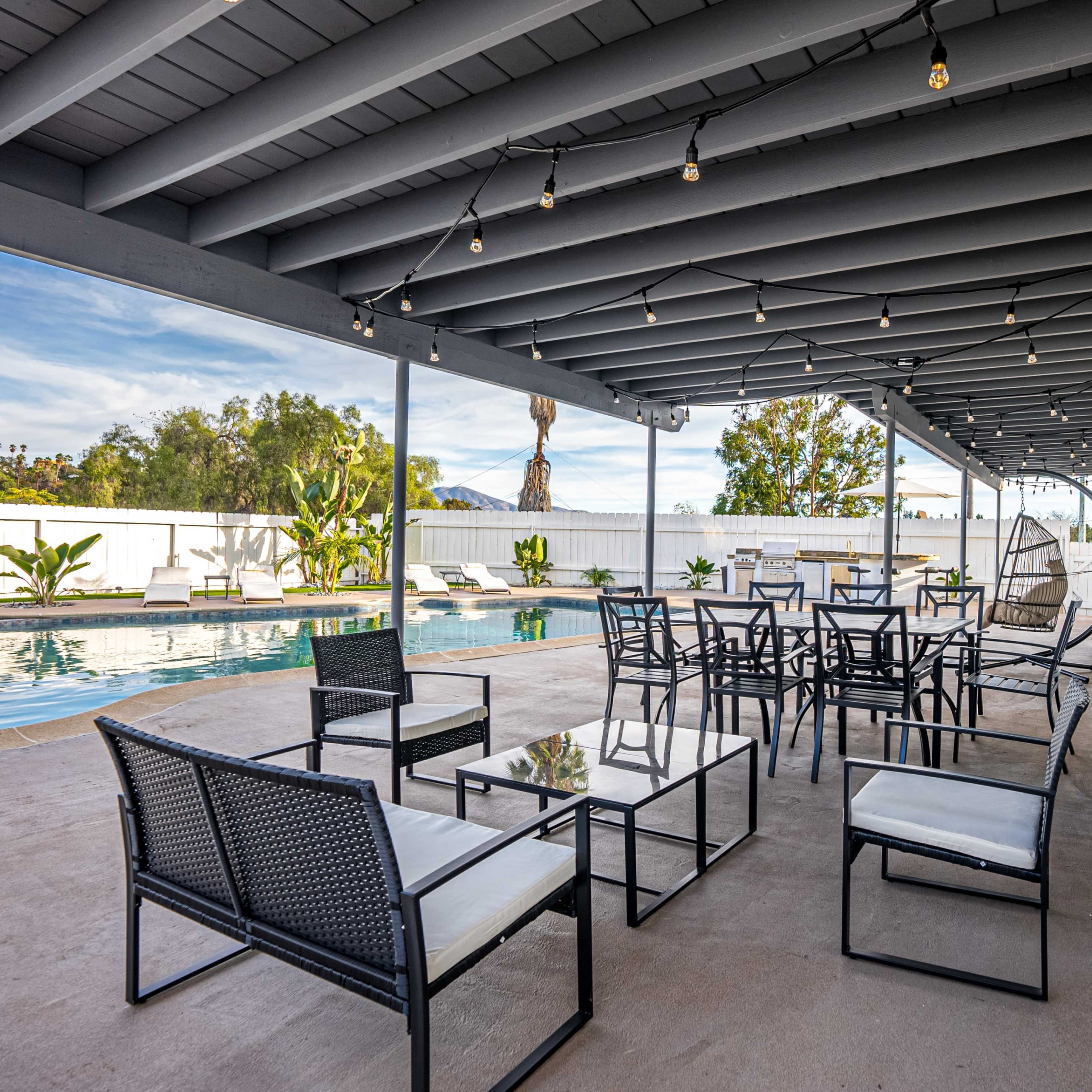 A covered patio area with seating and tables near a swimming pool.