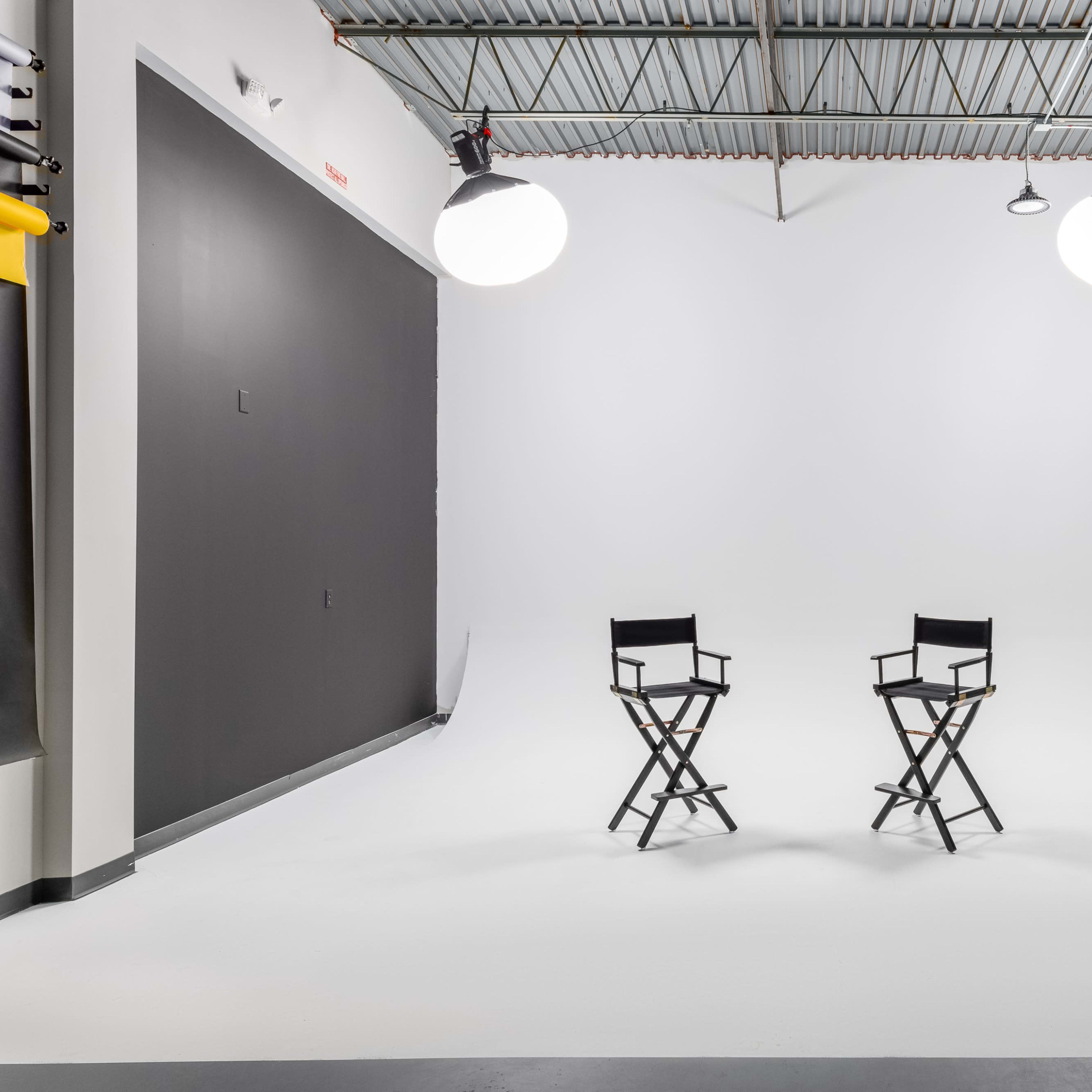A minimalist photography studio with two black director's chairs positioned on a white backdrop.