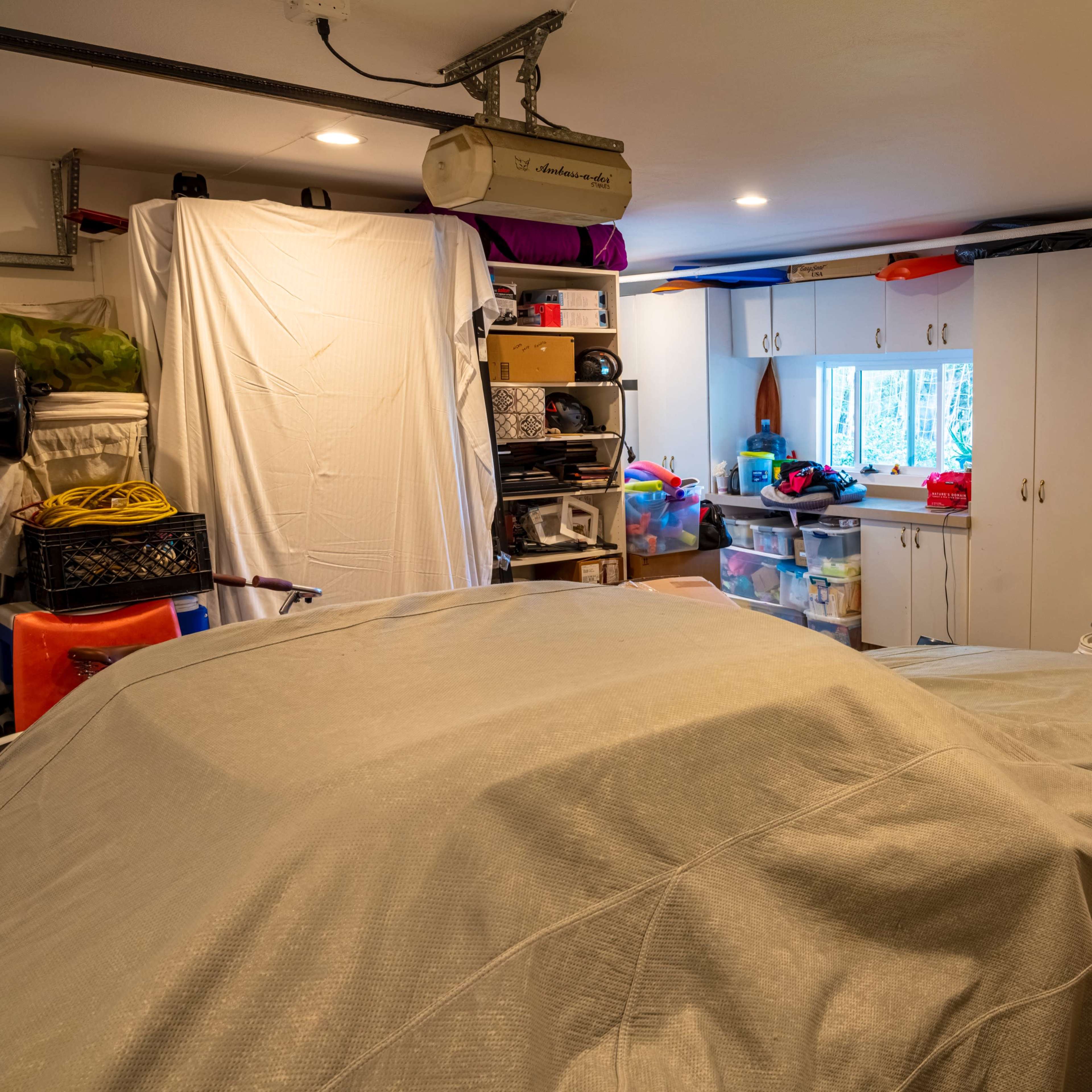 A garage is filled with covered vehicles, storage boxes, and appliances, including a washing machine and dryer.