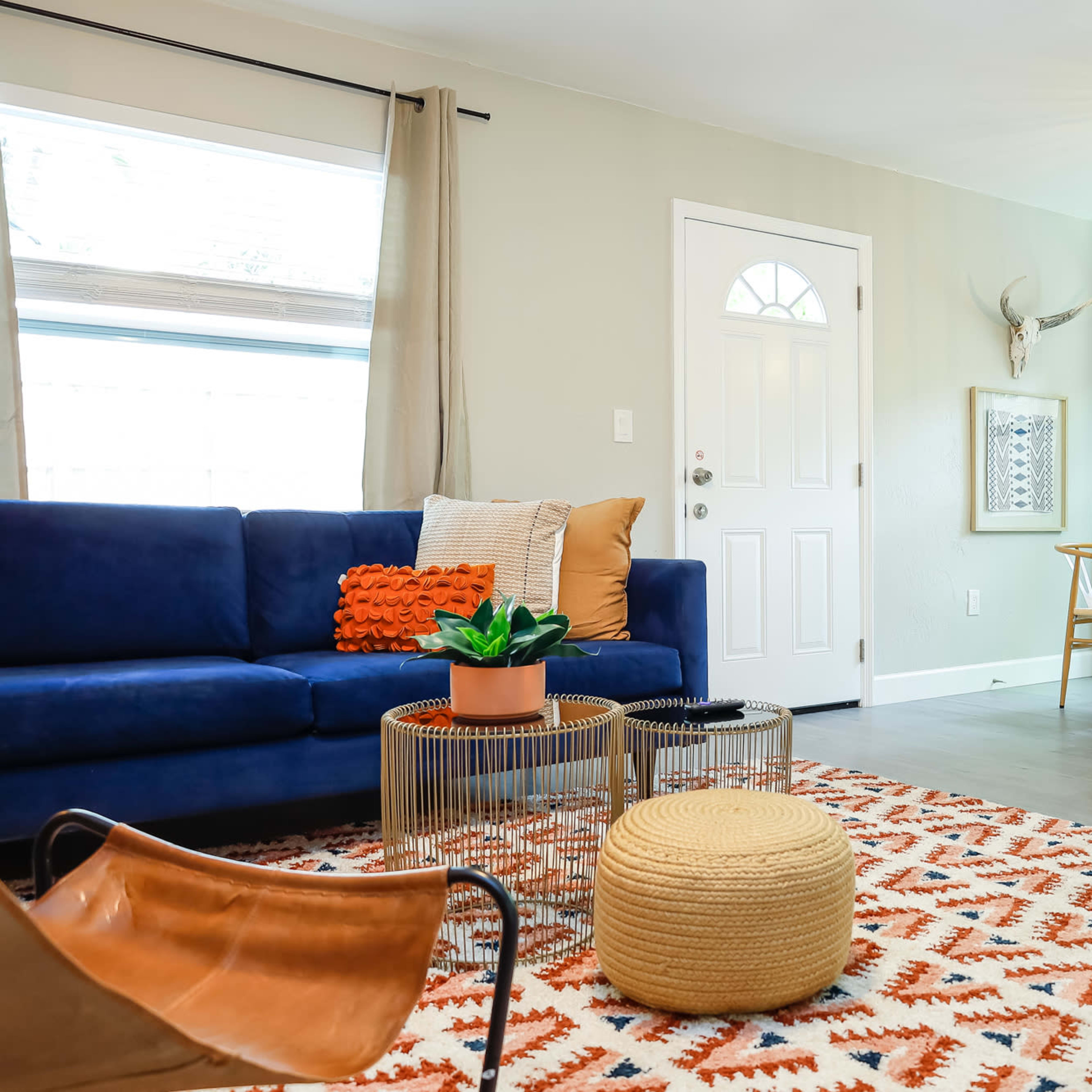 A bright living room features a blue couch, a dining area with wooden chairs, and a patterned rug.