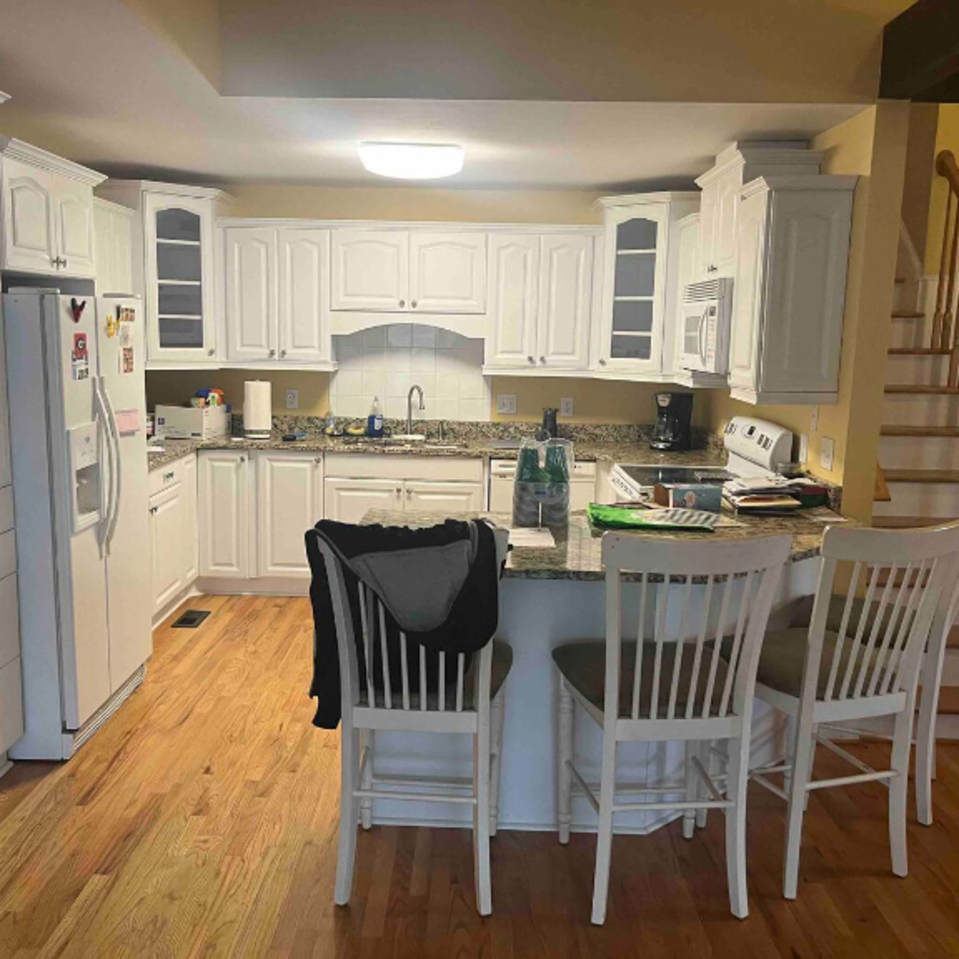 A modern kitchen with white cabinets, a central island with seating, and wooden flooring.