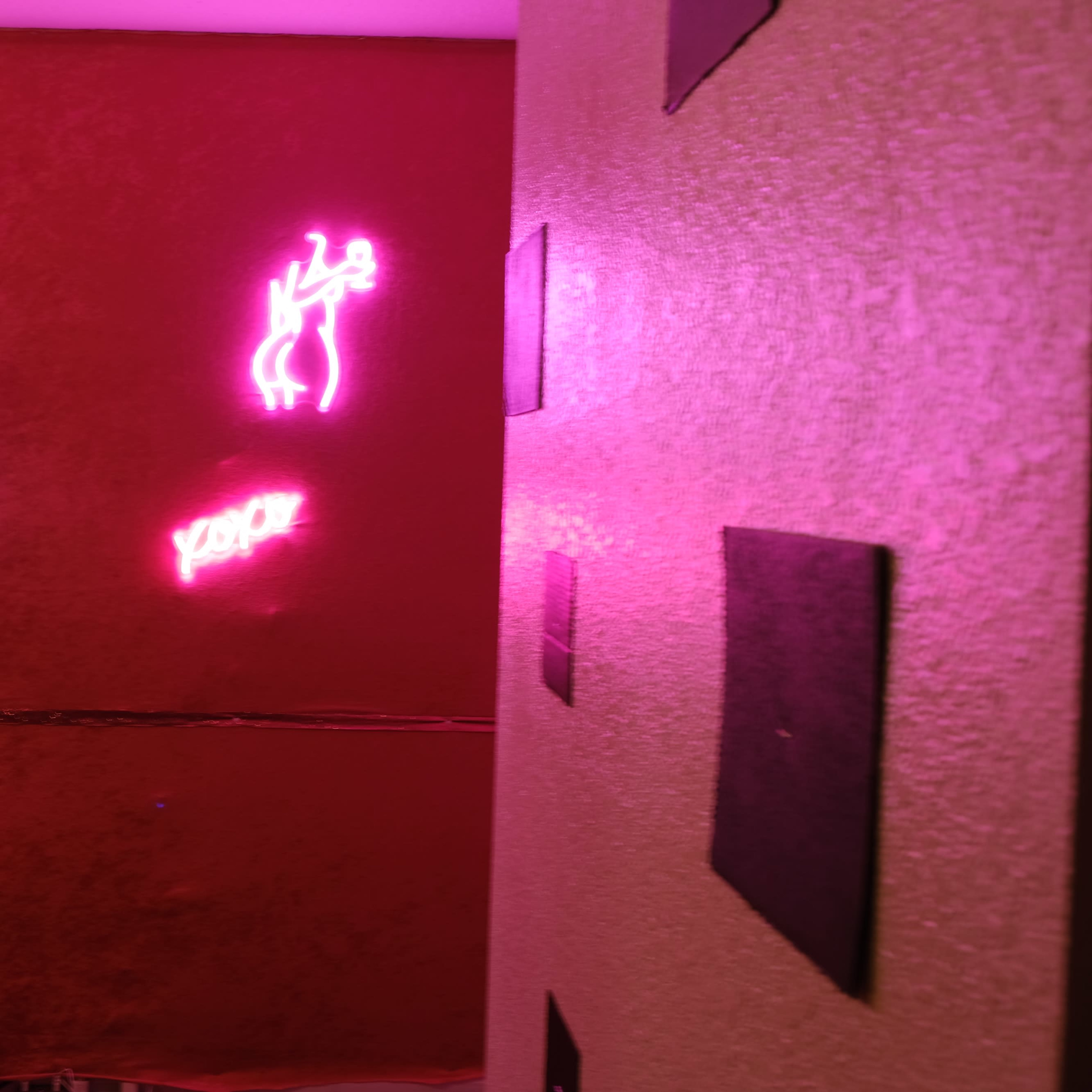 A room with red walls featuring pink neon signs illuminated against the surface.