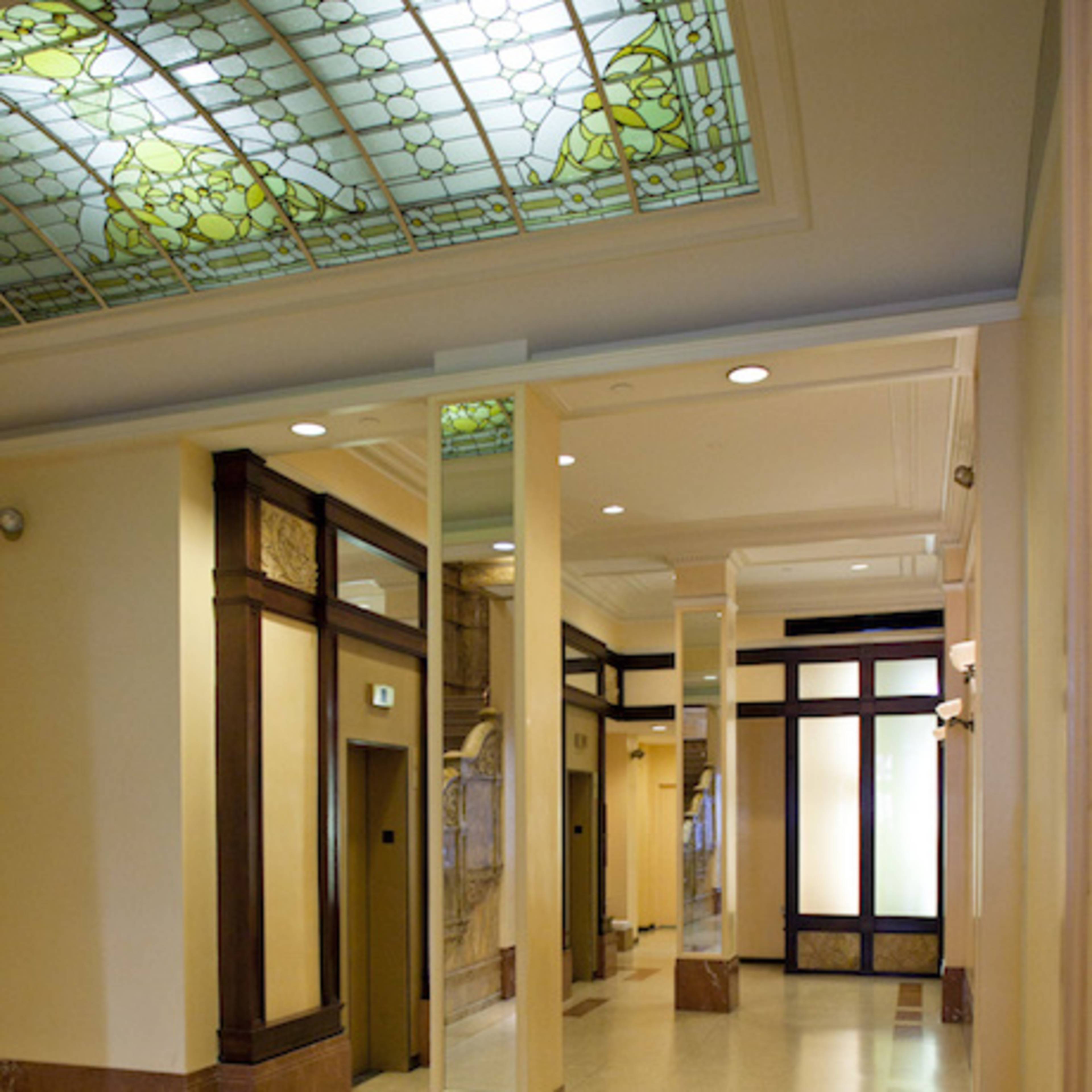 A hallway in a building featuring a stained glass ceiling, elevators, and polished stone flooring.