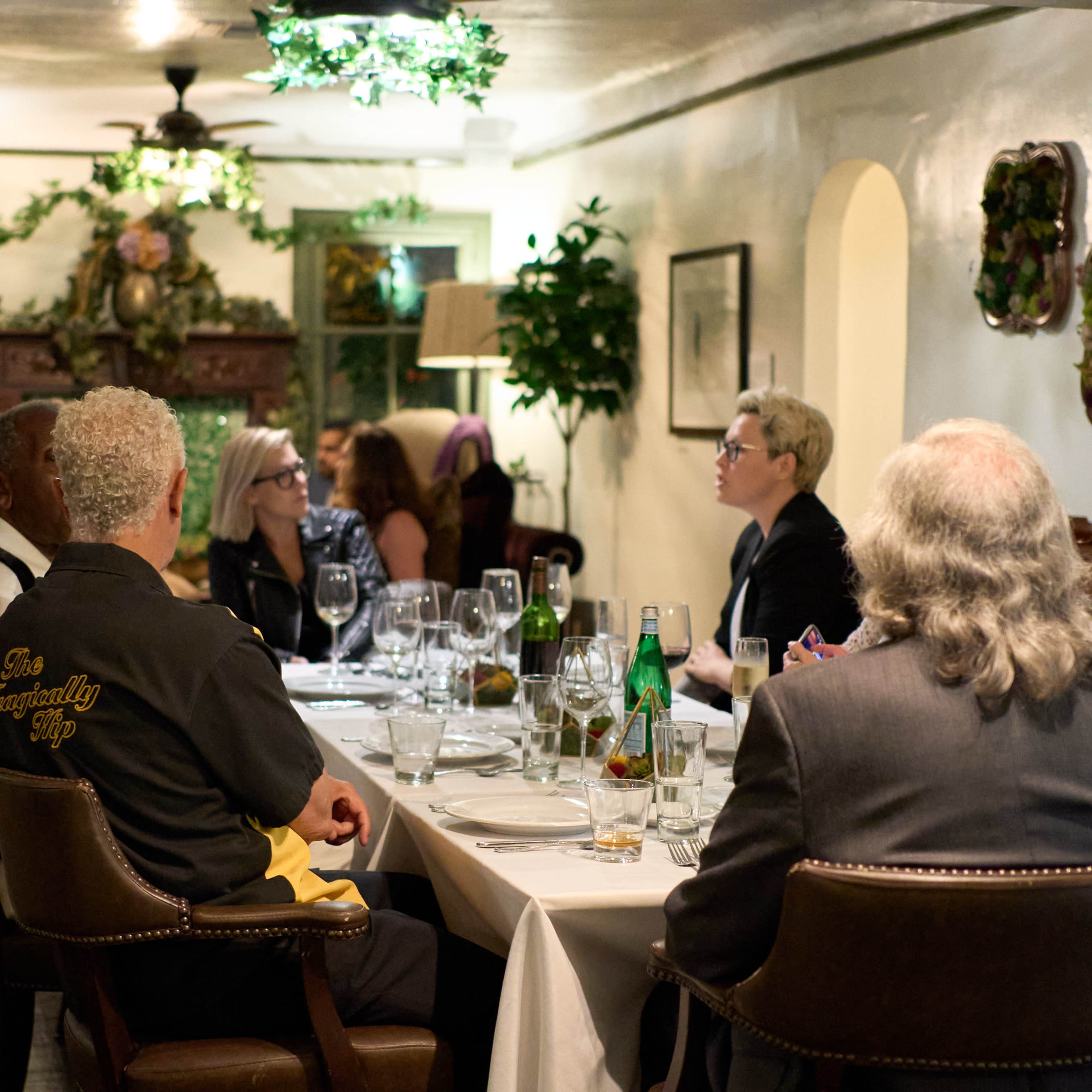 A group of six people sits at a dining table in an elegantly decorated restaurant with flowers and plants.