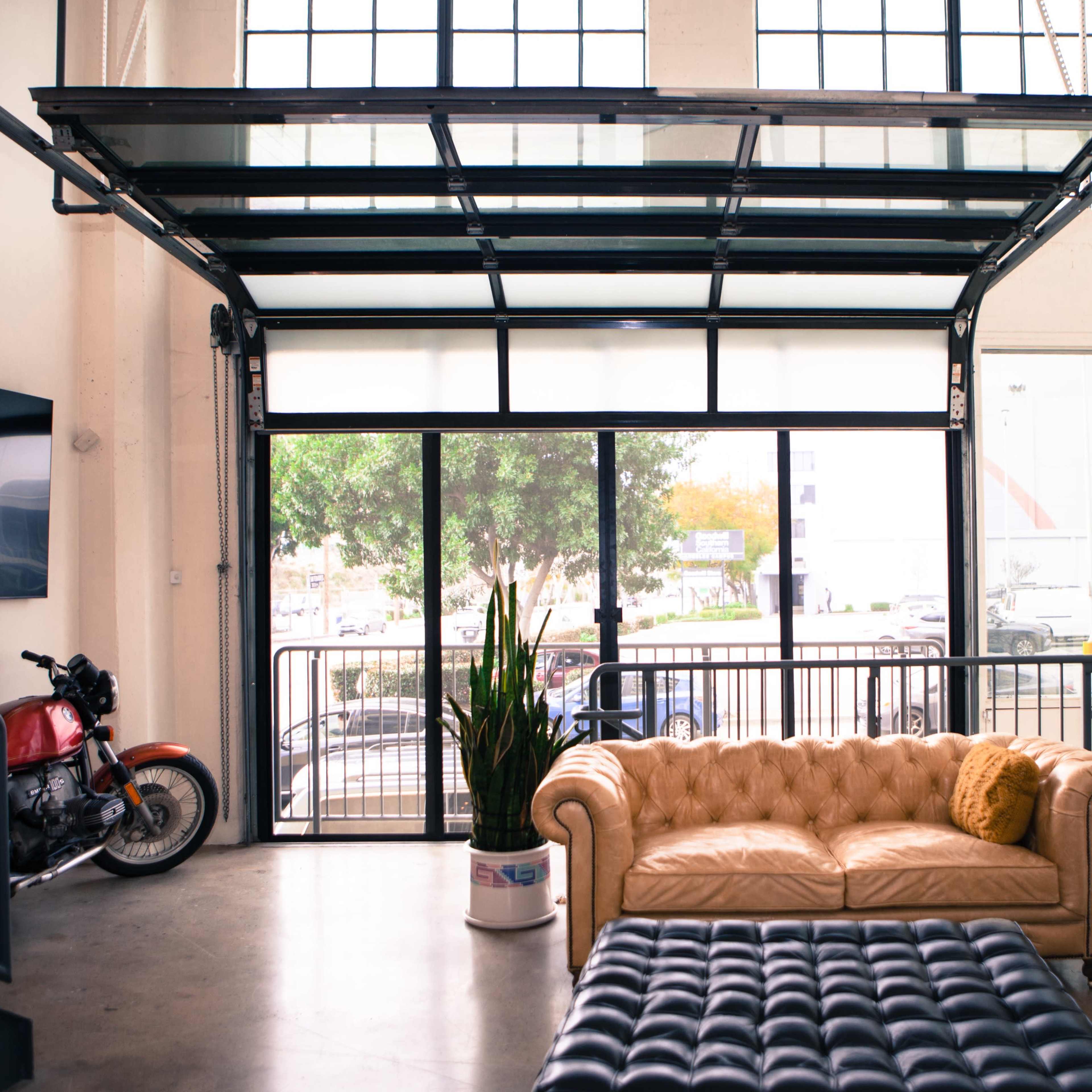 A spacious room with large windows, a beige leather sofa, a dark brown leather couch, and a motorcycle parked near the entrance.