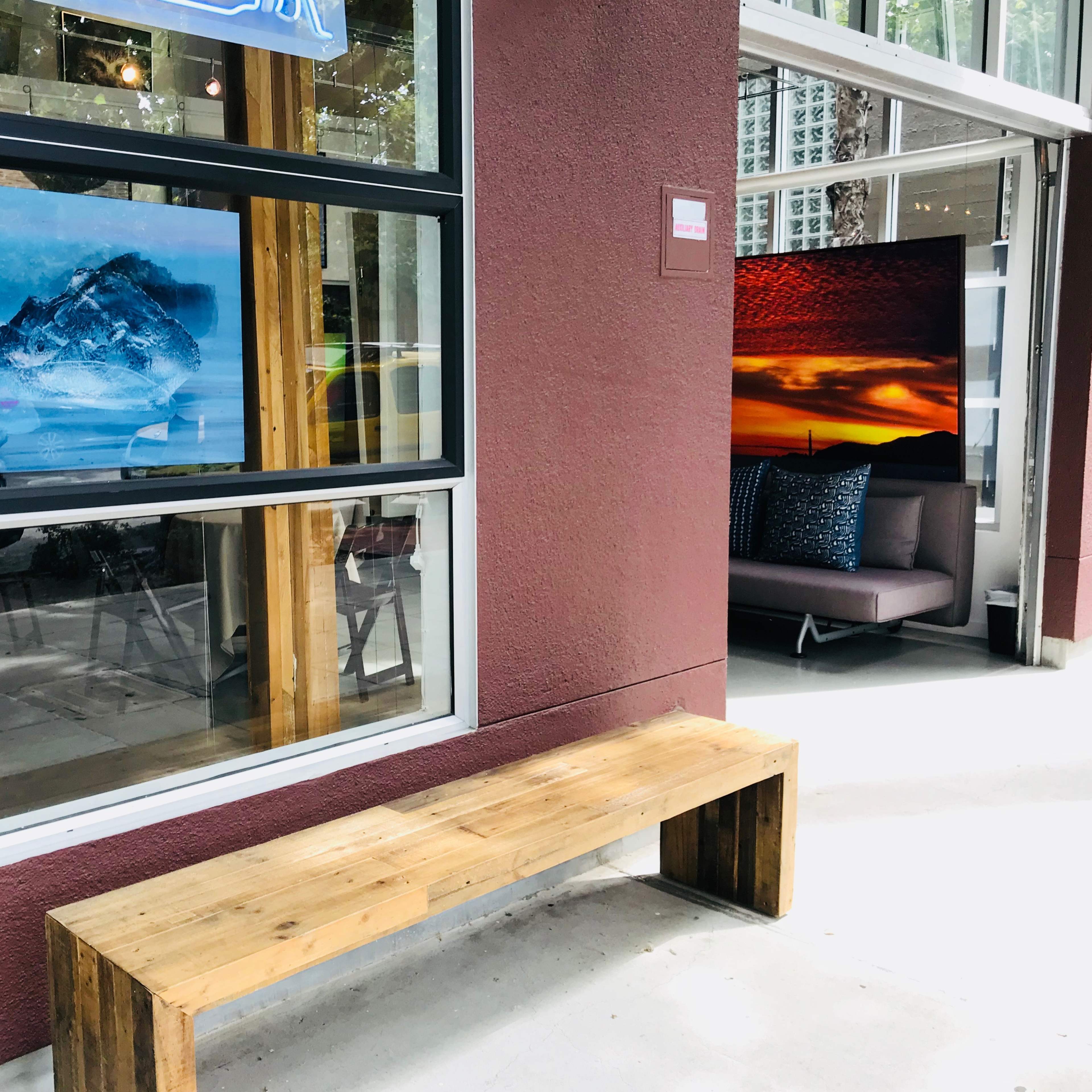 A wooden bench situated outside a building with large windows displaying landscape artwork.