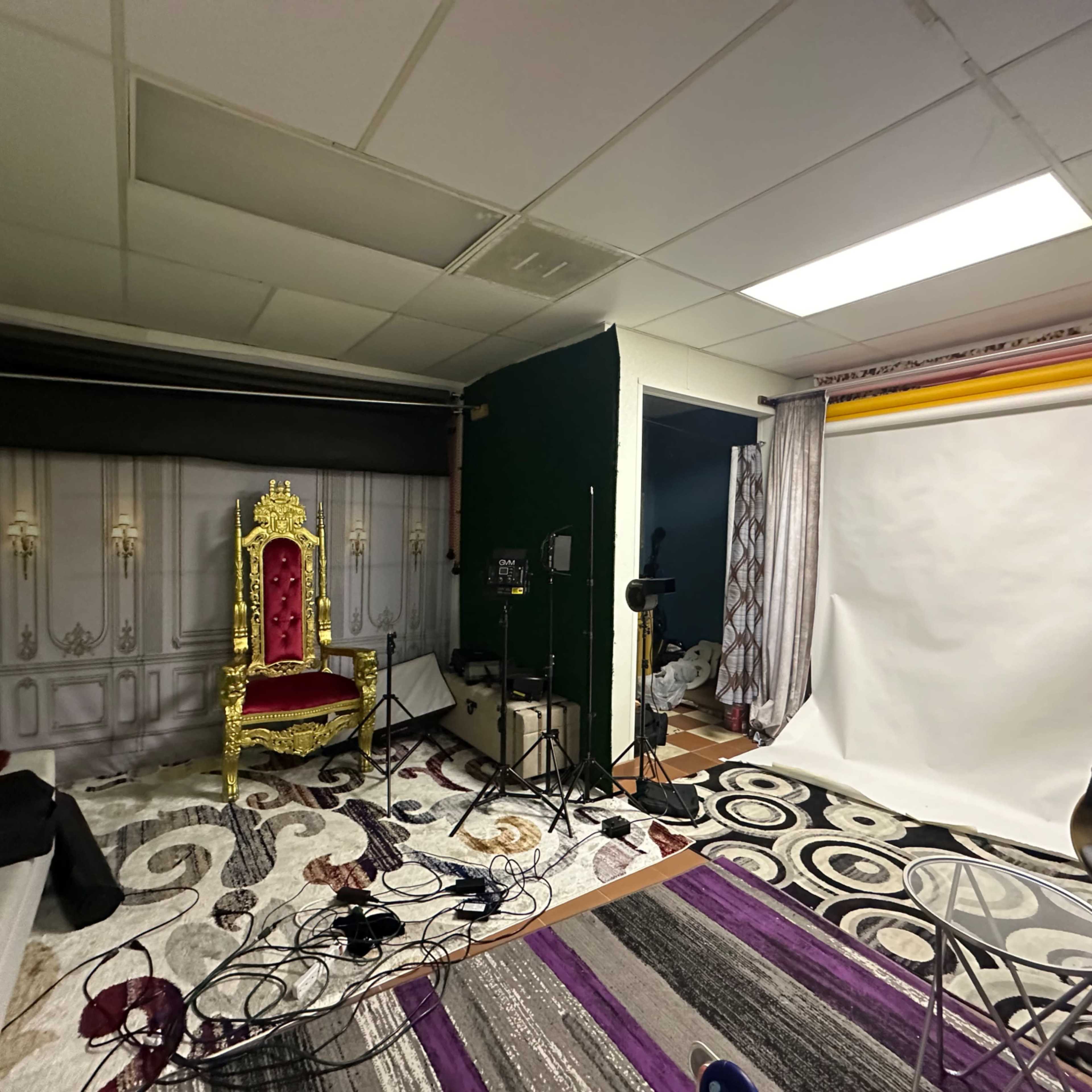 A photography studio setup with a golden throne, backdrop stands, cables, and various props scattered on the floor.