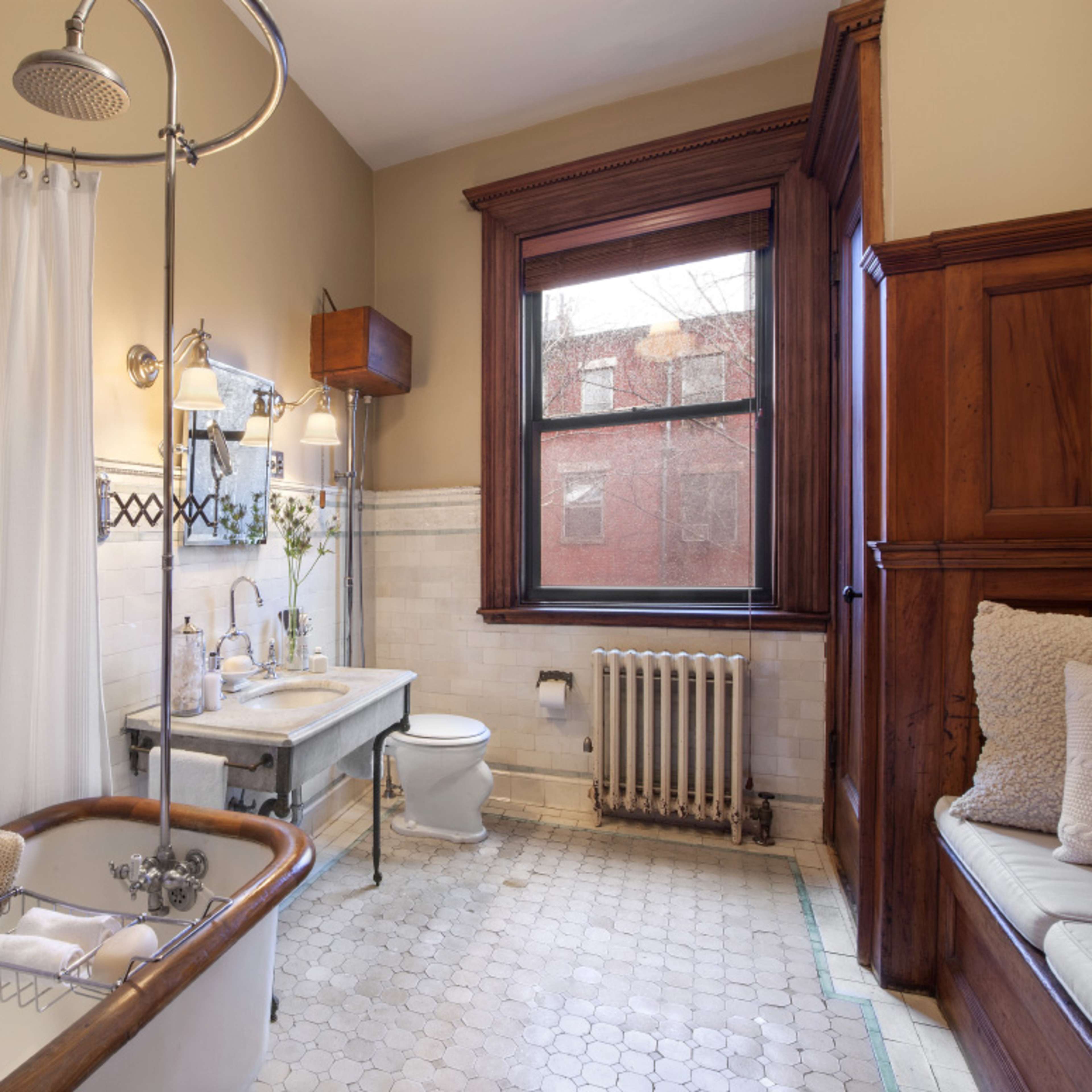 The bathroom features a vintage clawfoot tub, a pedestal sink, and a window with wooden trim overlooking a brick exterior.