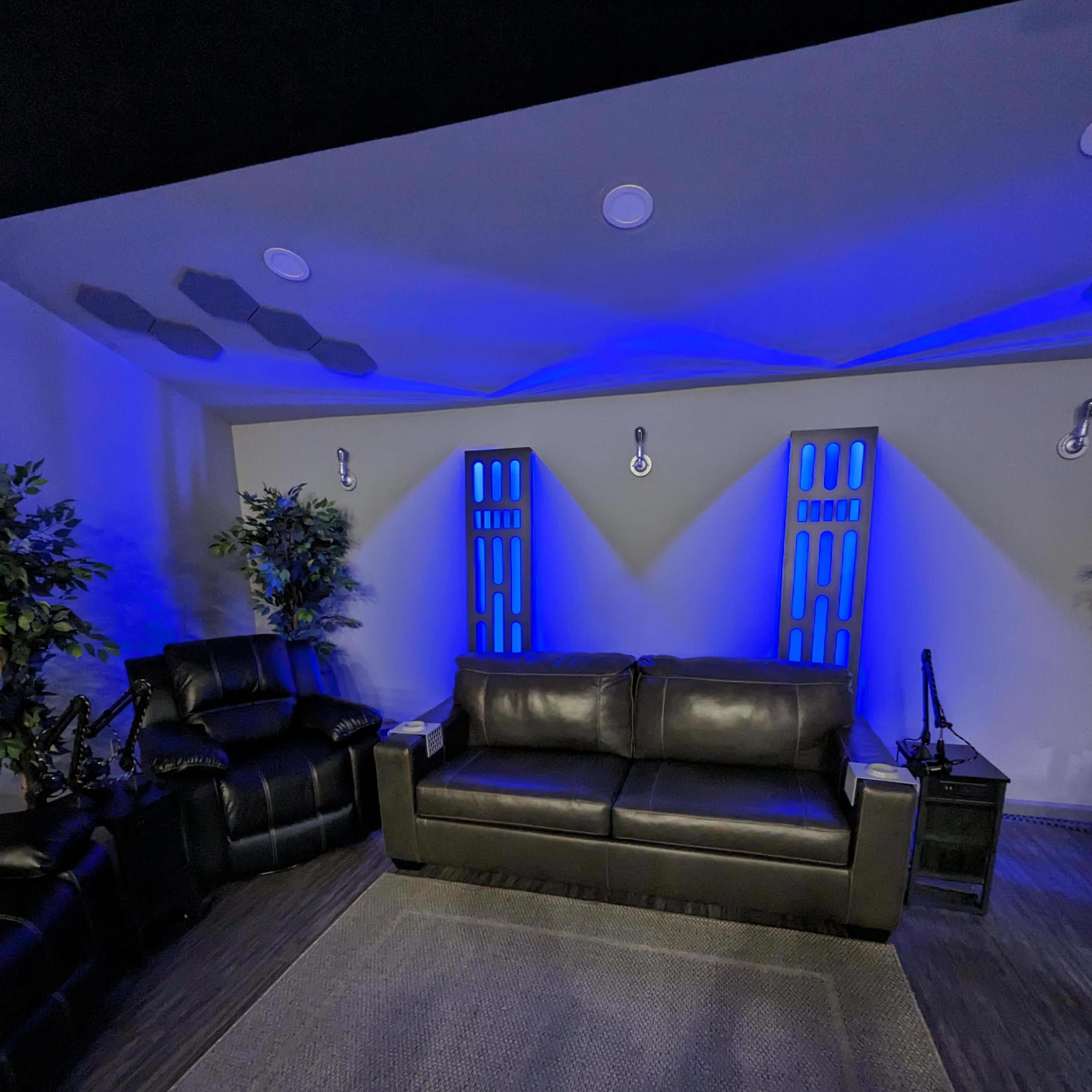 A modern lounge area with a black leather sofa, a recliner, and blue accent lighting against the walls.