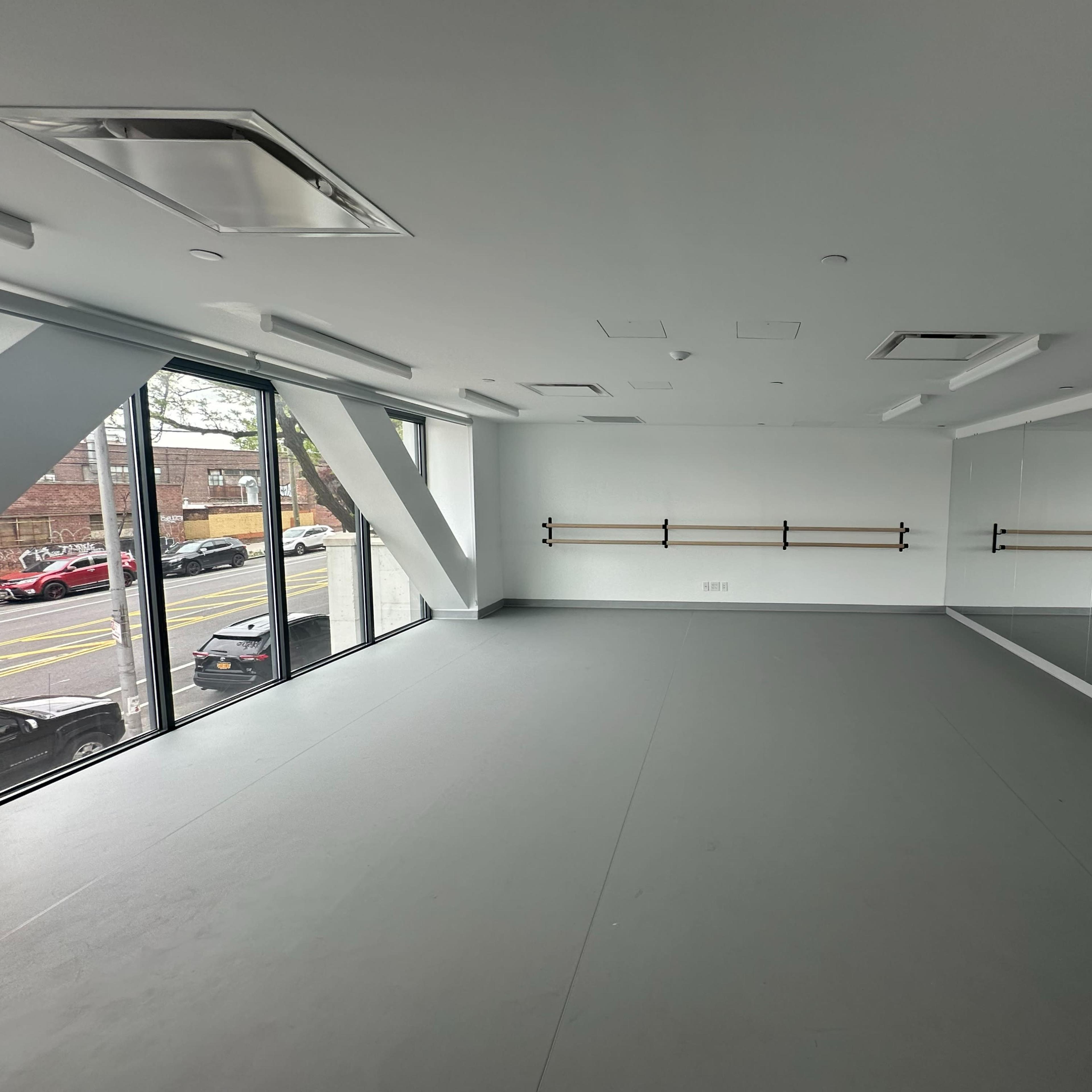 A spacious, unoccupied studio with large windows and mirrors on one wall.