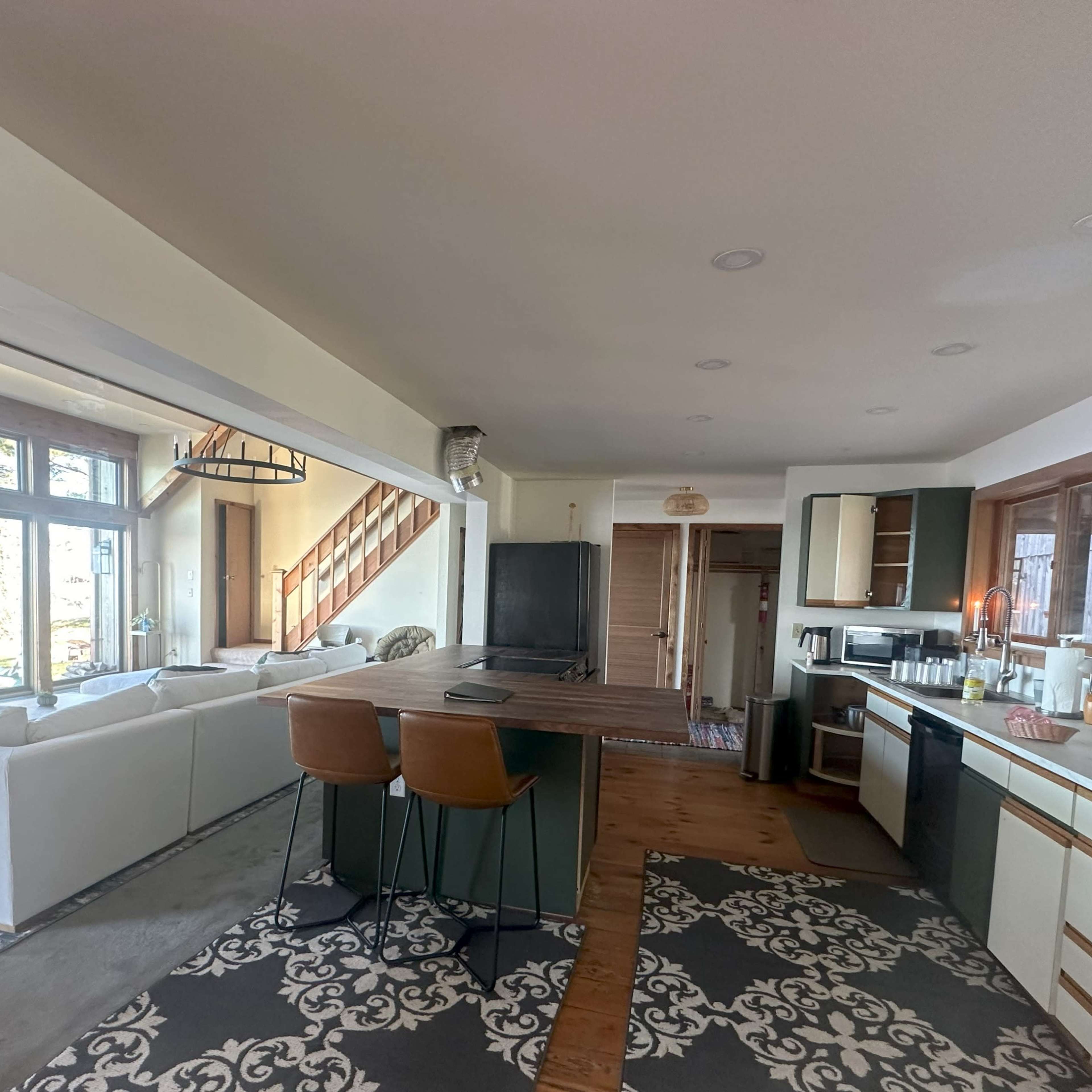 A spacious, modern kitchen and living area with a large island, seating for two, and a staircase leading to an upper level.