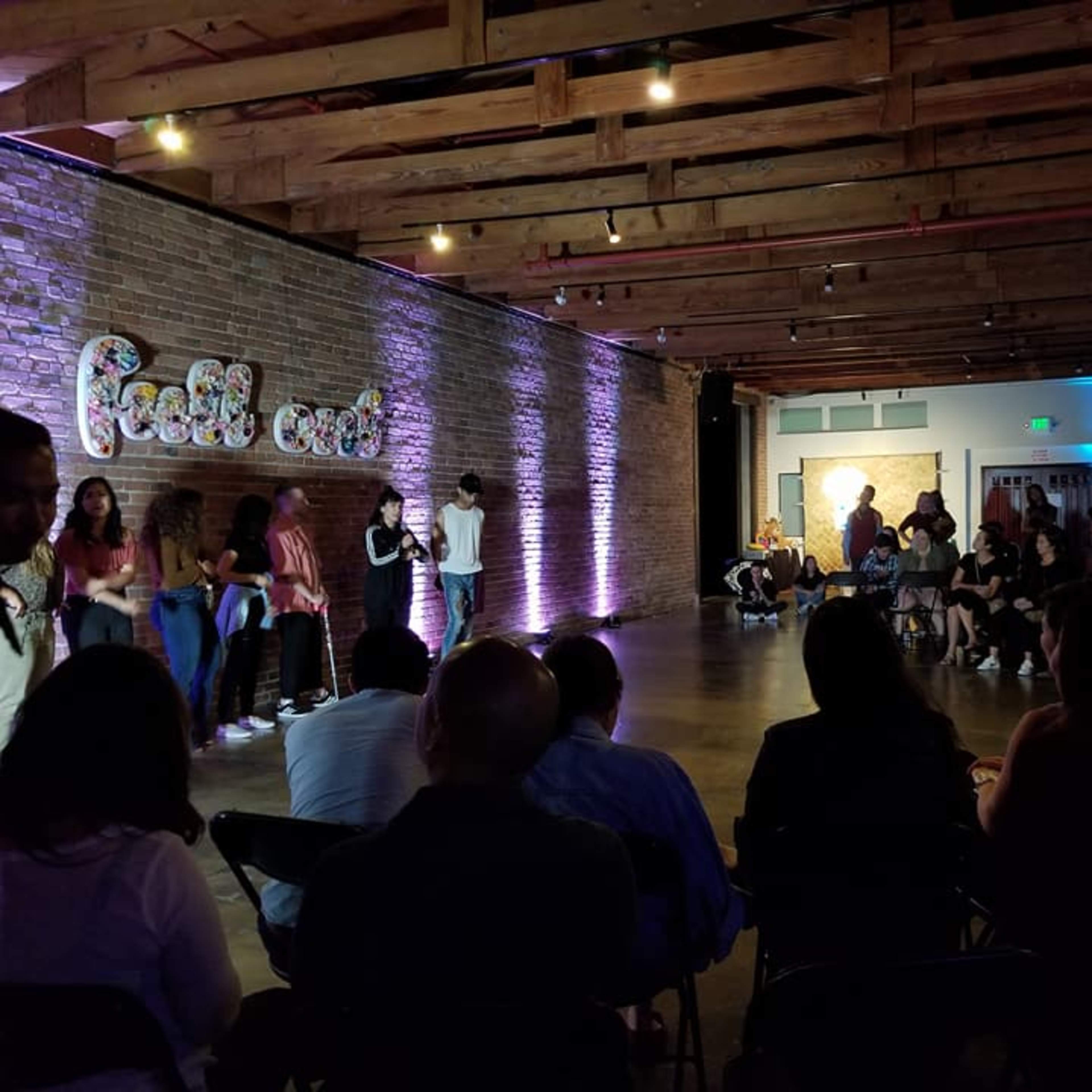 A crowd gathers in a well-lit space with exposed brick walls for a performance or event.