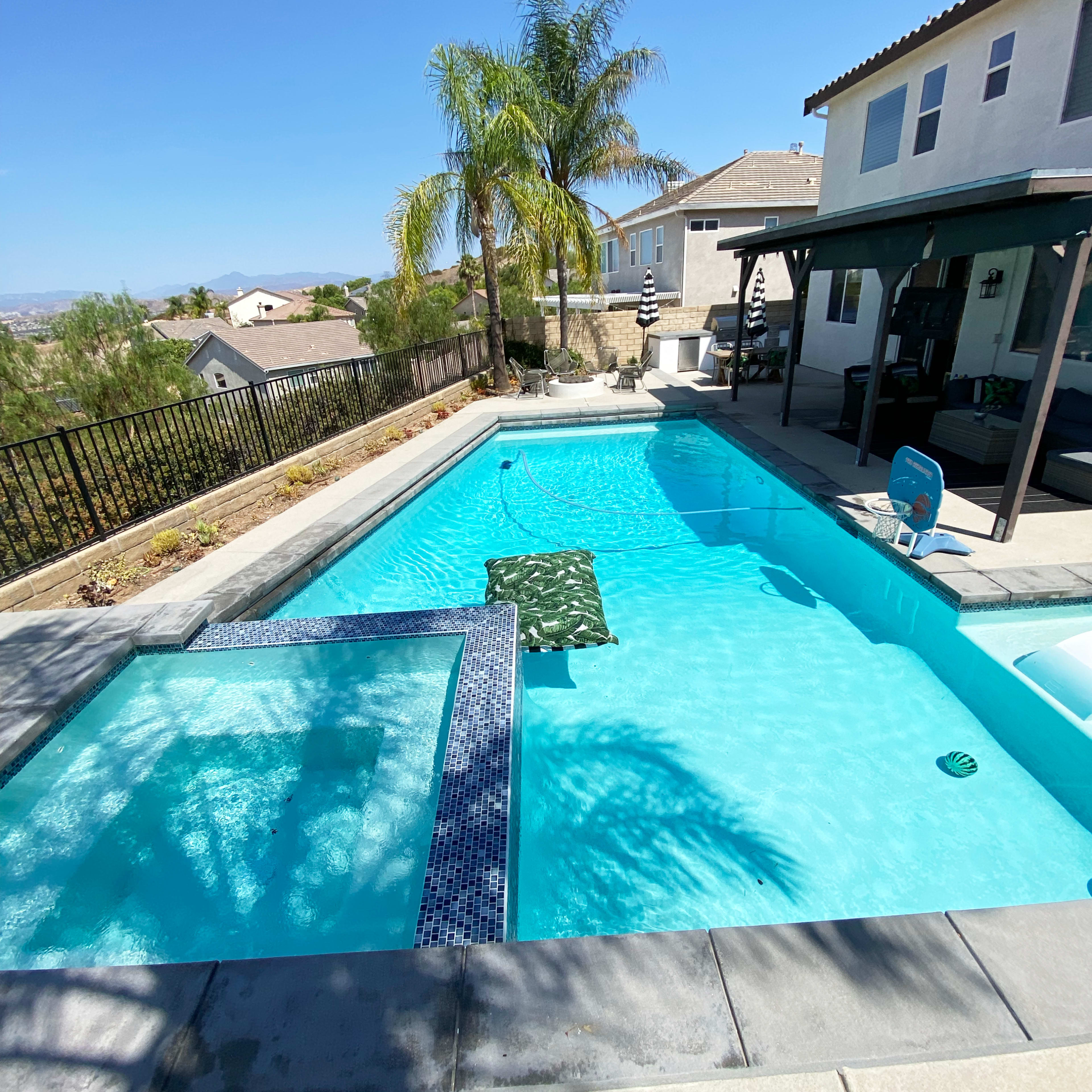 A rectangular swimming pool surrounded by a patio and a view of houses and hills in the background.
