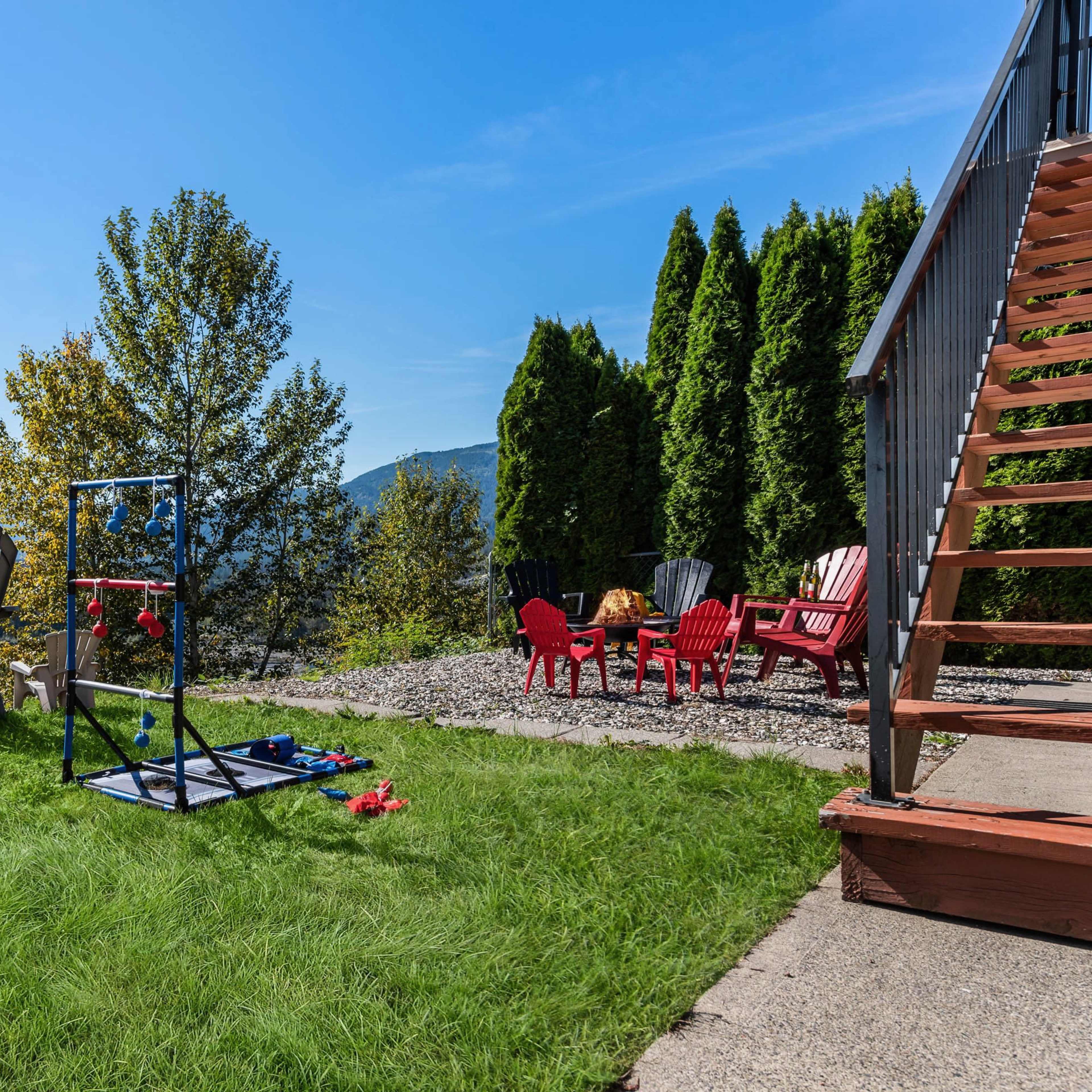 A grassy area with chairs and a ladder leading to a building, set against a backdrop of mountains and trees under a clear blue sky.