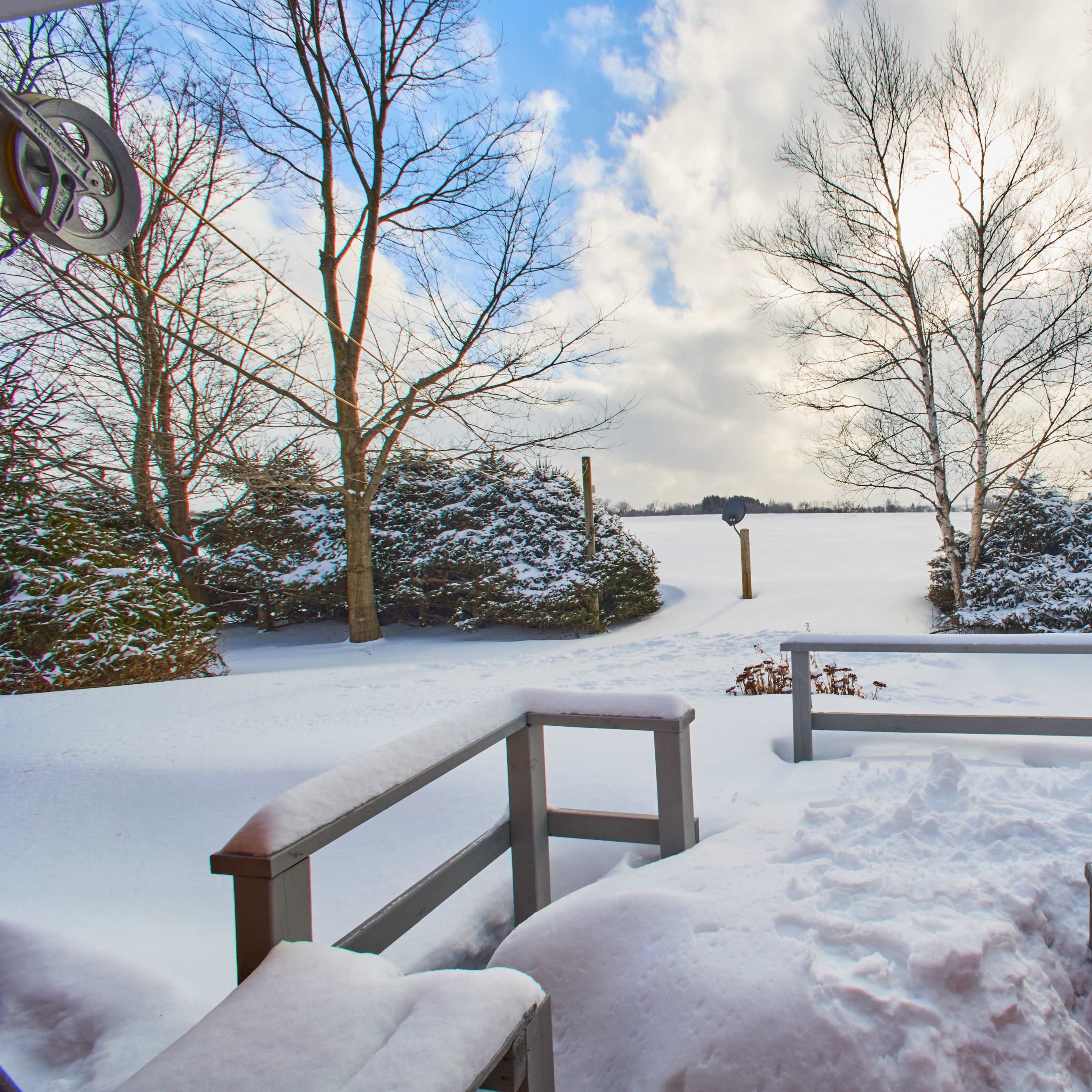 A snowy landscape is visible from a wooden deck, with trees surrounding a frozen lake under a partly cloudy sky.