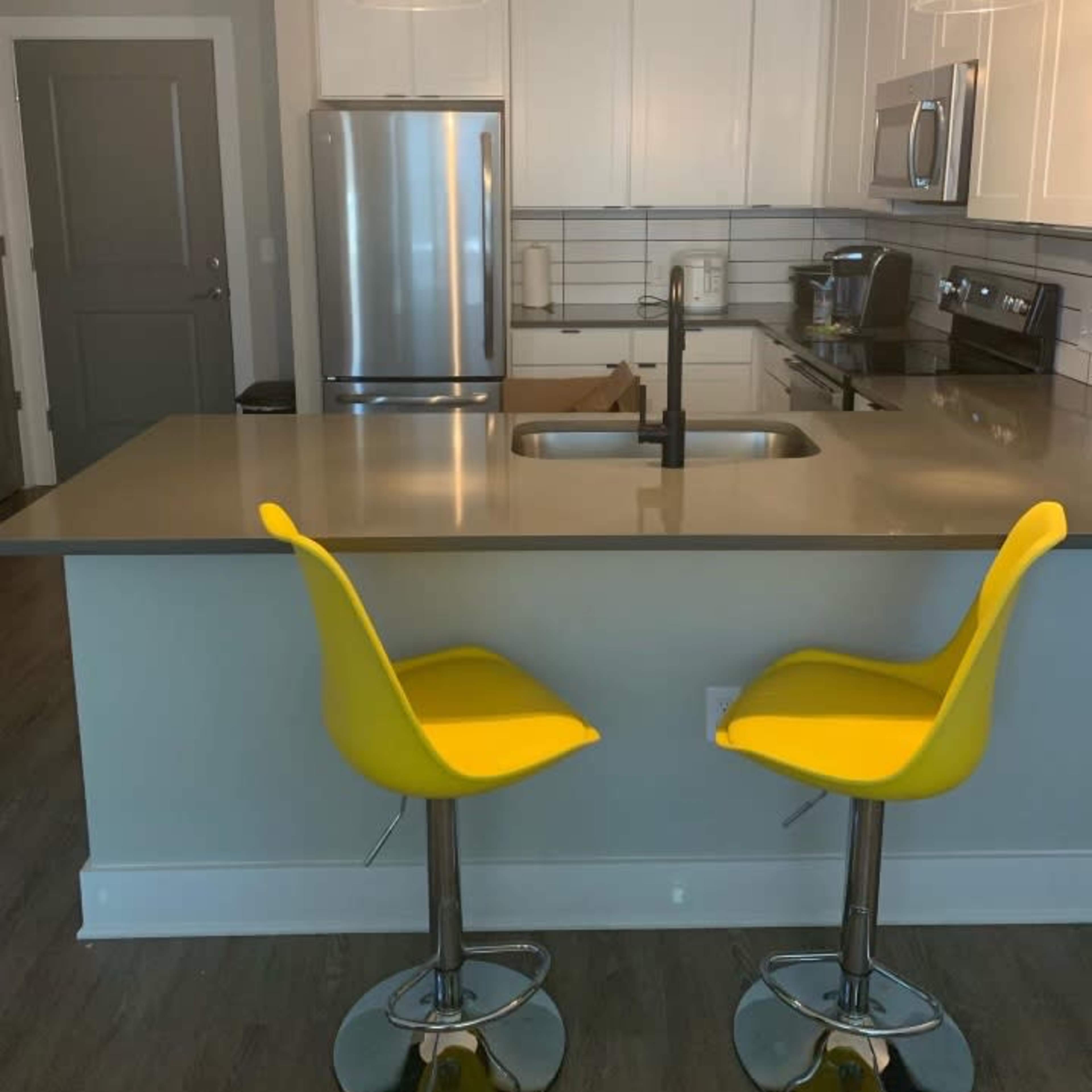 A modern kitchen features stainless steel appliances, white cabinetry, and two yellow bar stools at the island.
