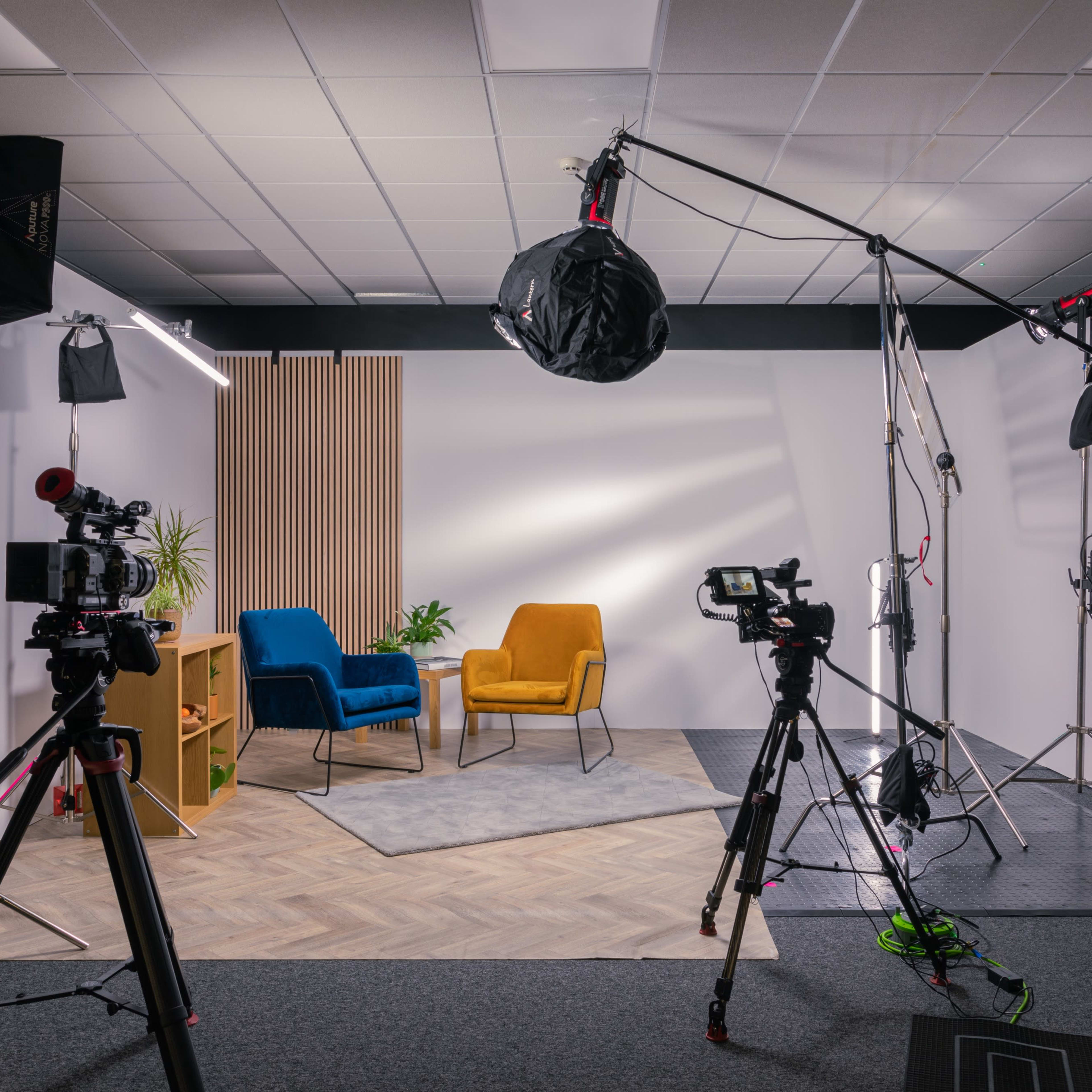 A video production studio is set up with two chairs, a plant, and various lighting and camera equipment arranged around the space.
