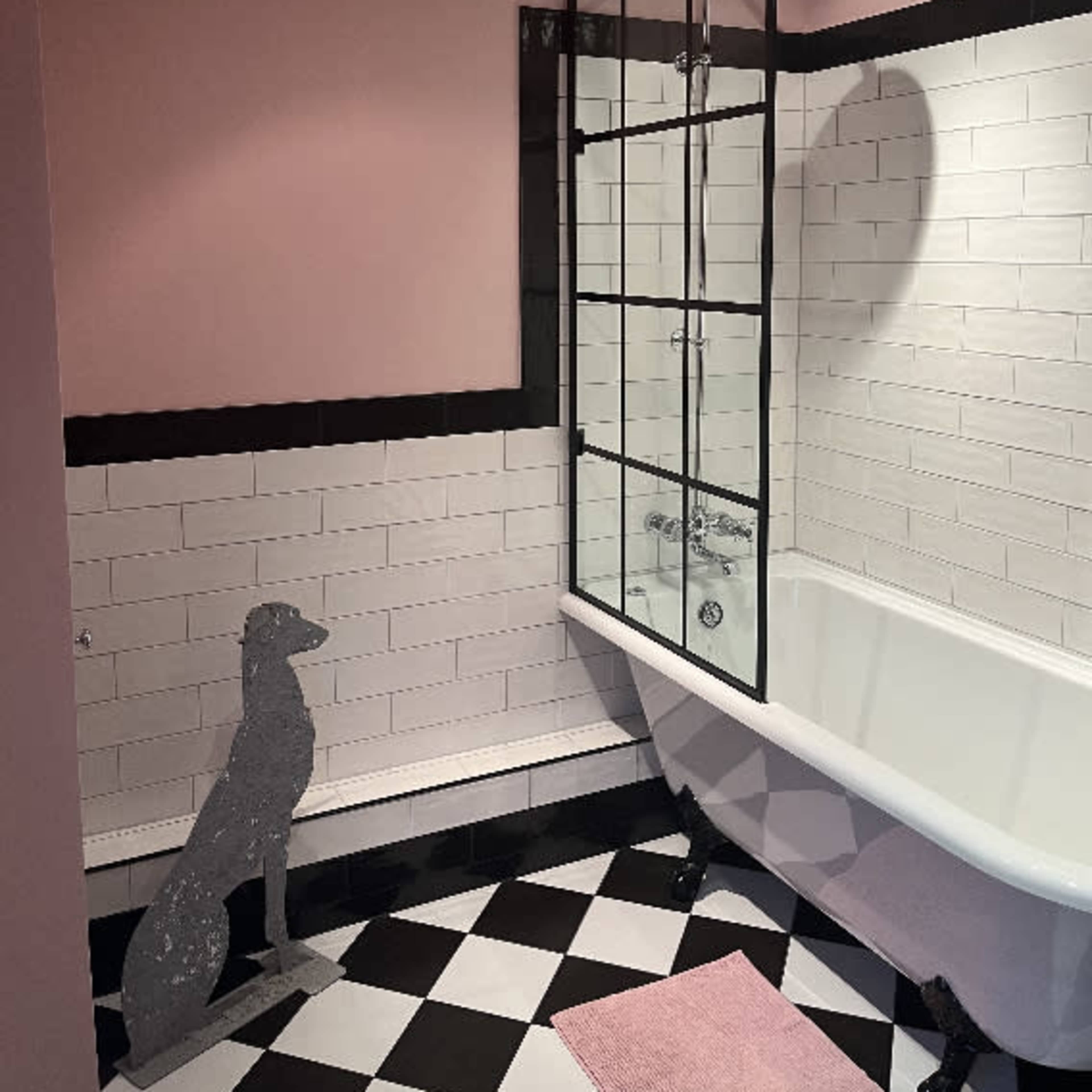 A bathroom featuring a freestanding bathtub, a glass shower enclosure, black and white checkered floor tiles, and a pink accent wall.