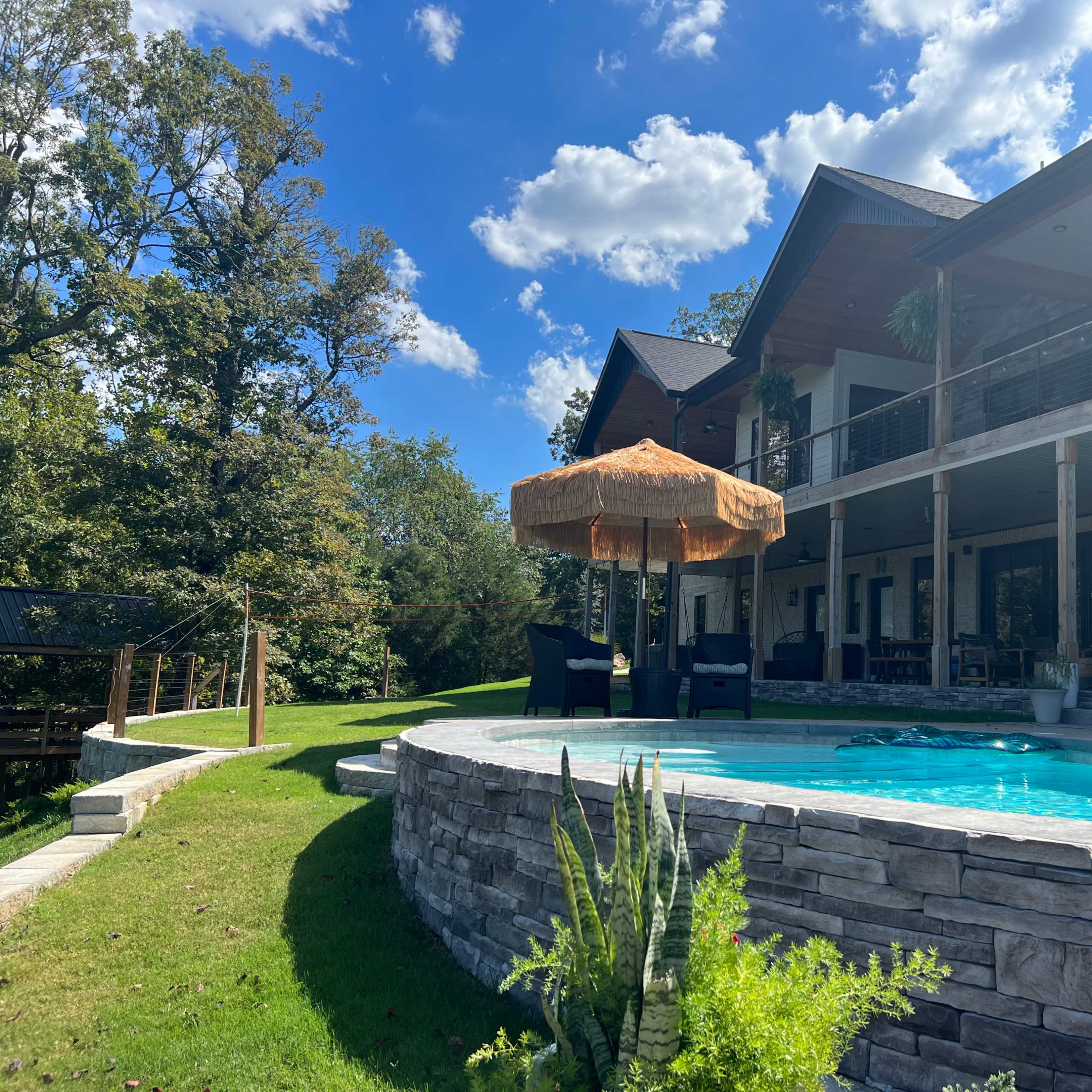 A modern house with a pool is set against a blue sky and surrounded by greenery.