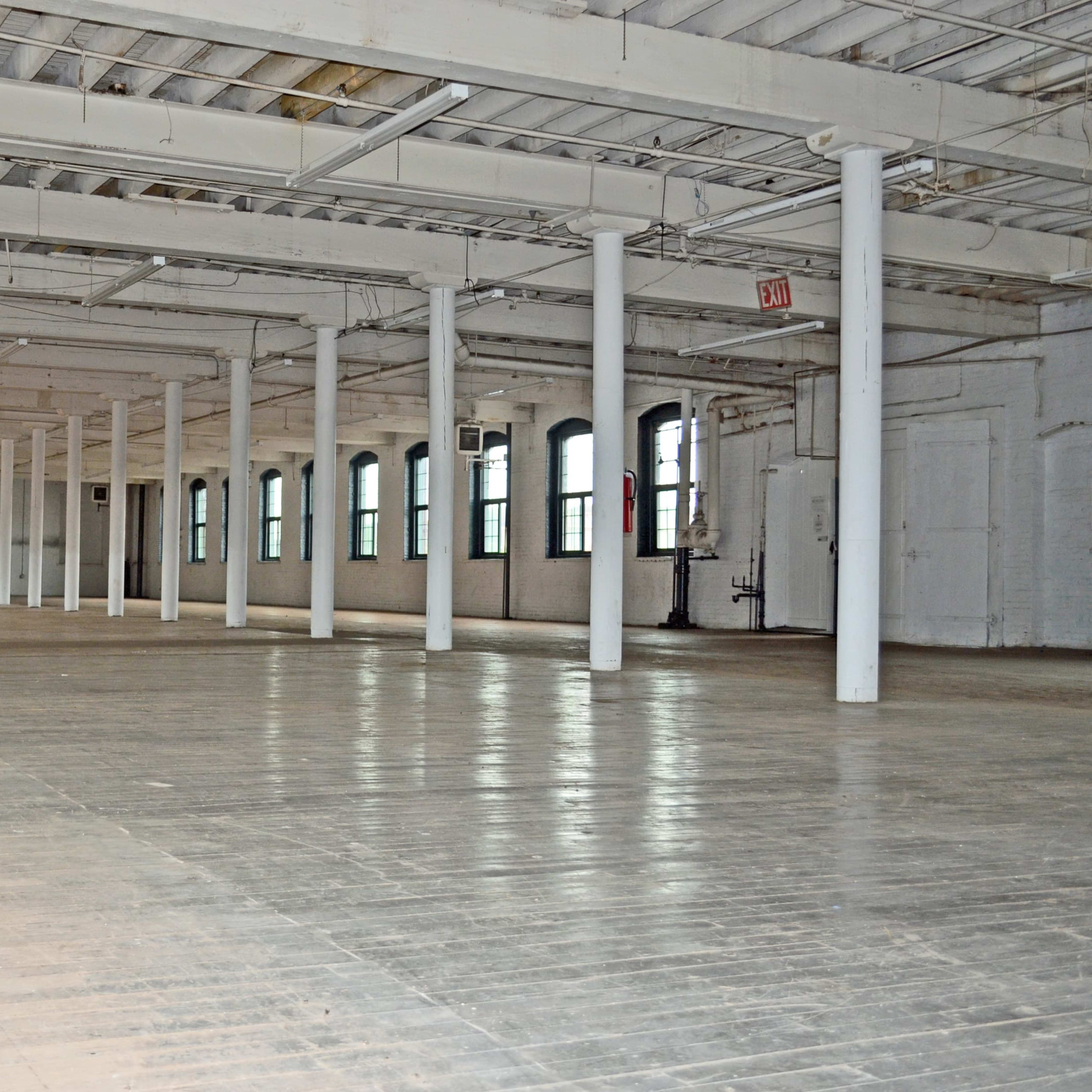 A spacious, empty industrial room with wooden flooring and concrete pillars.