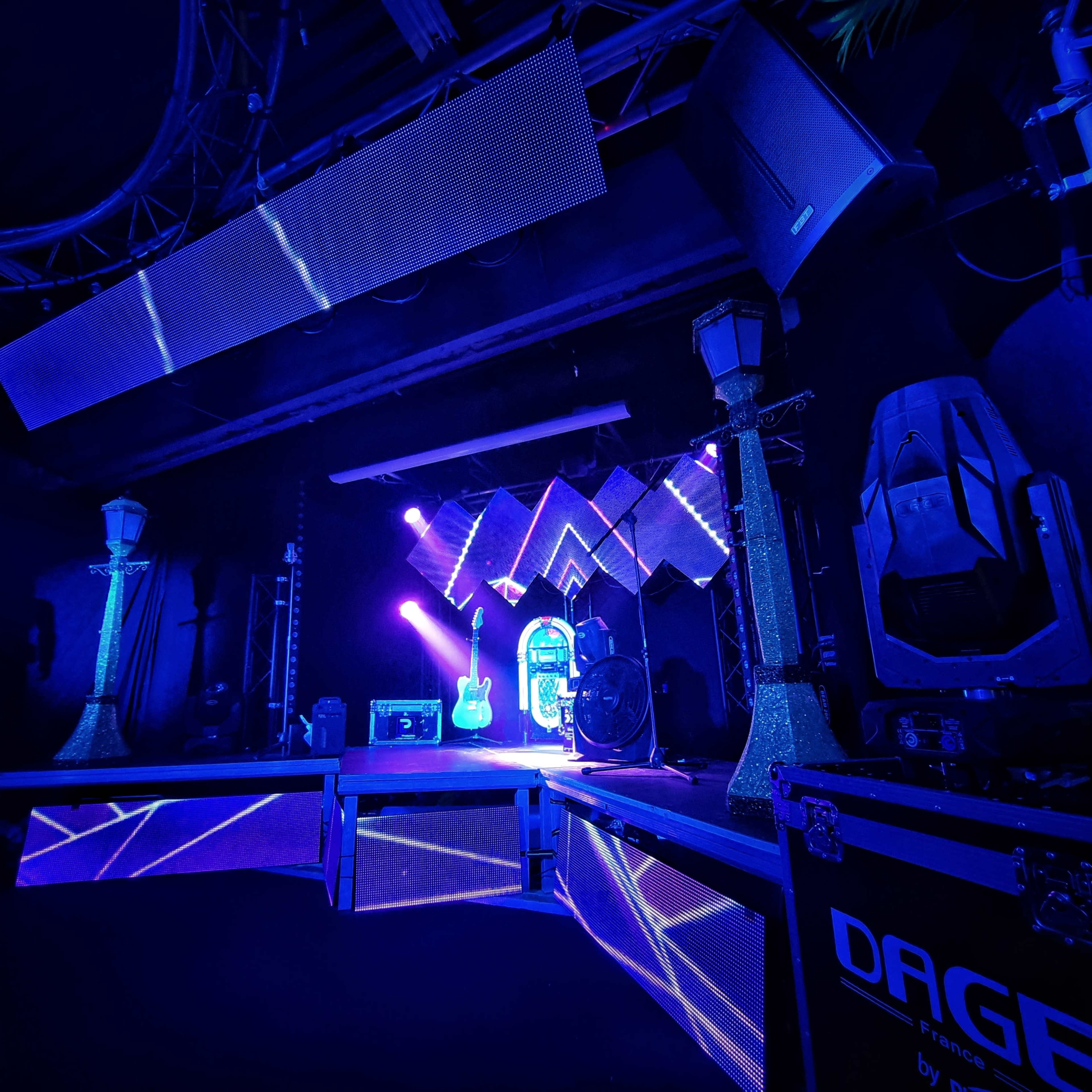 A stage setup featuring blue lighting, musical instruments, and various stage equipment in a darkened venue.