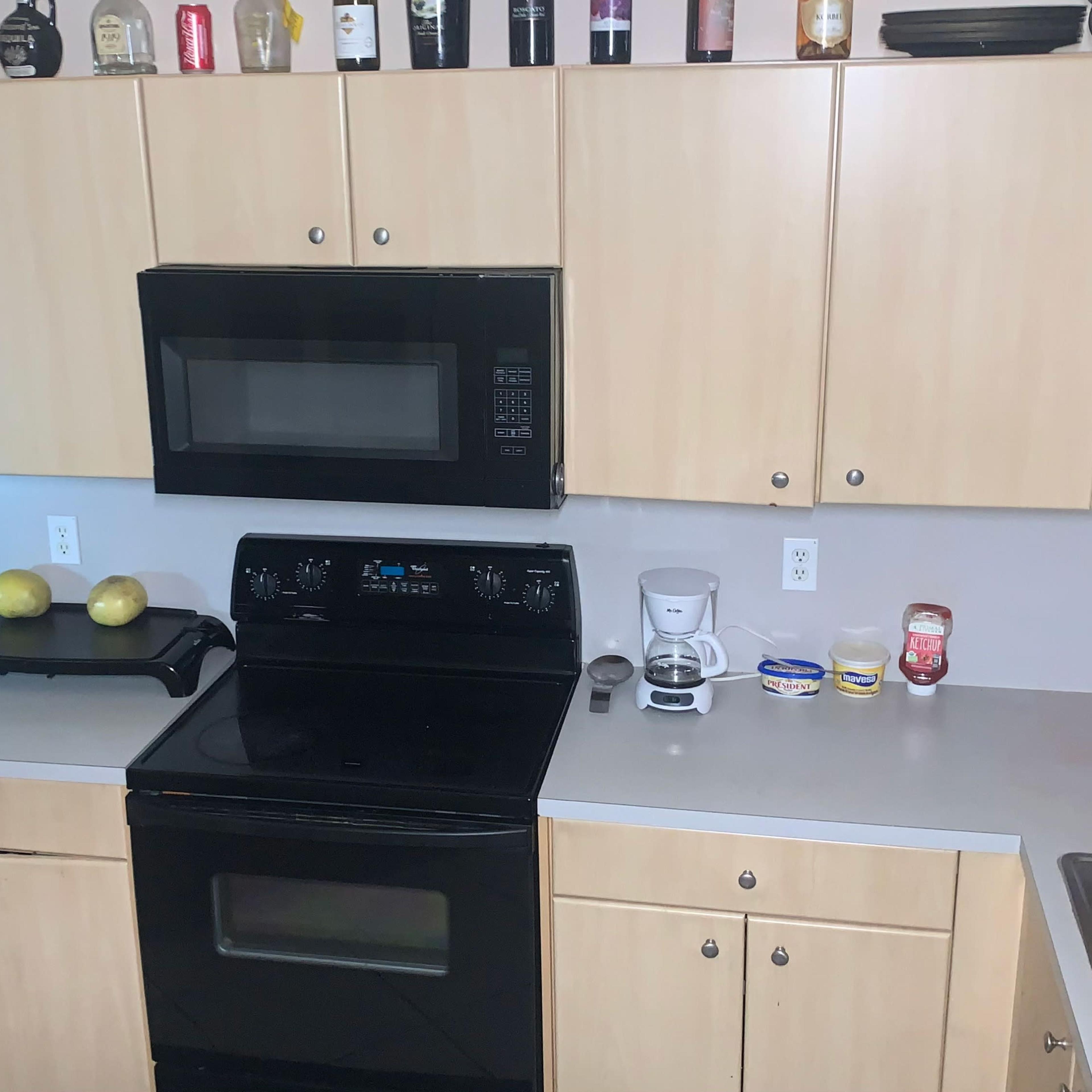 A kitchen with wooden cabinets, a black stove and microwave, and a countertop featuring various condiments and kitchen appliances.