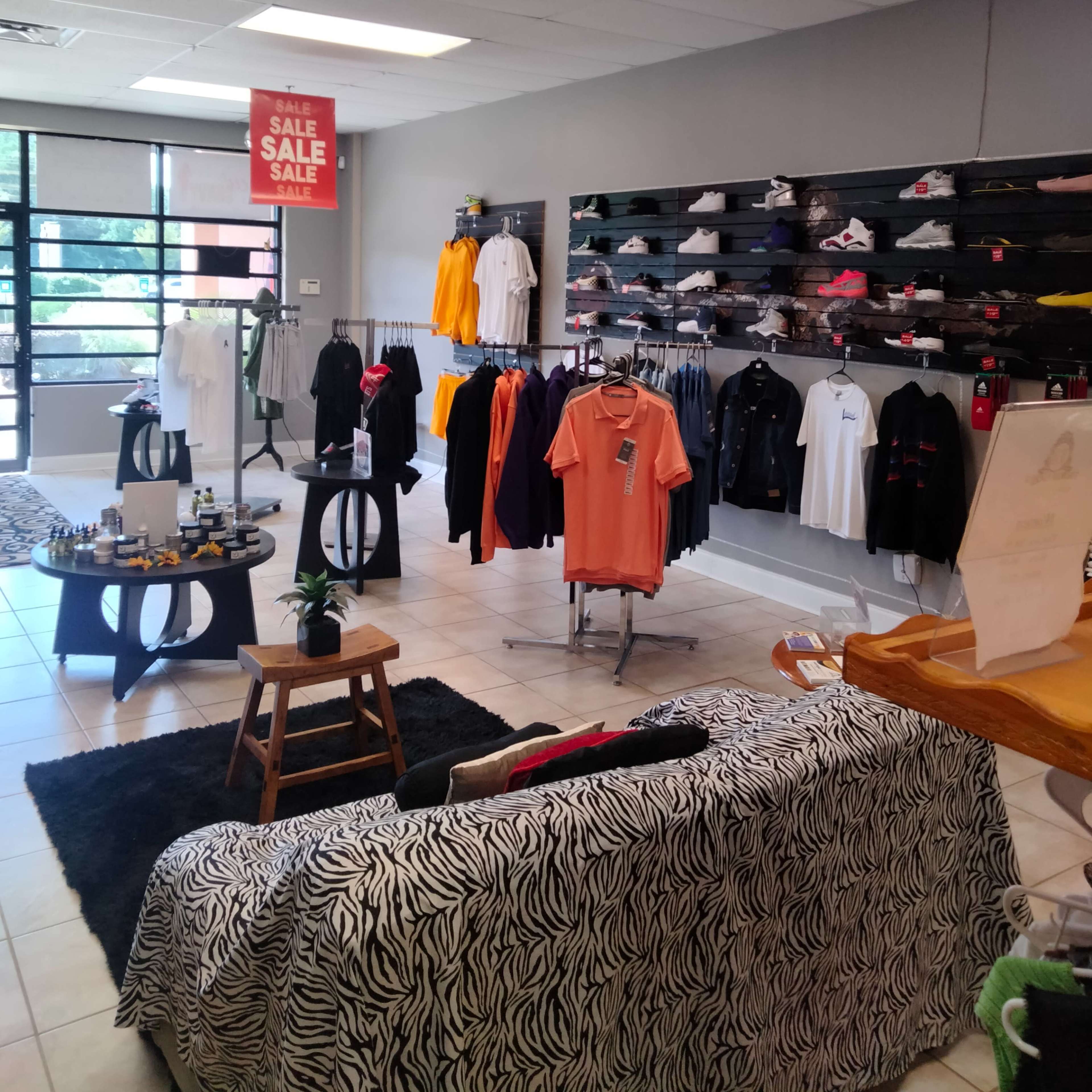 A clothing store interior with racks of apparel, a seating area, and promotional sale signage.