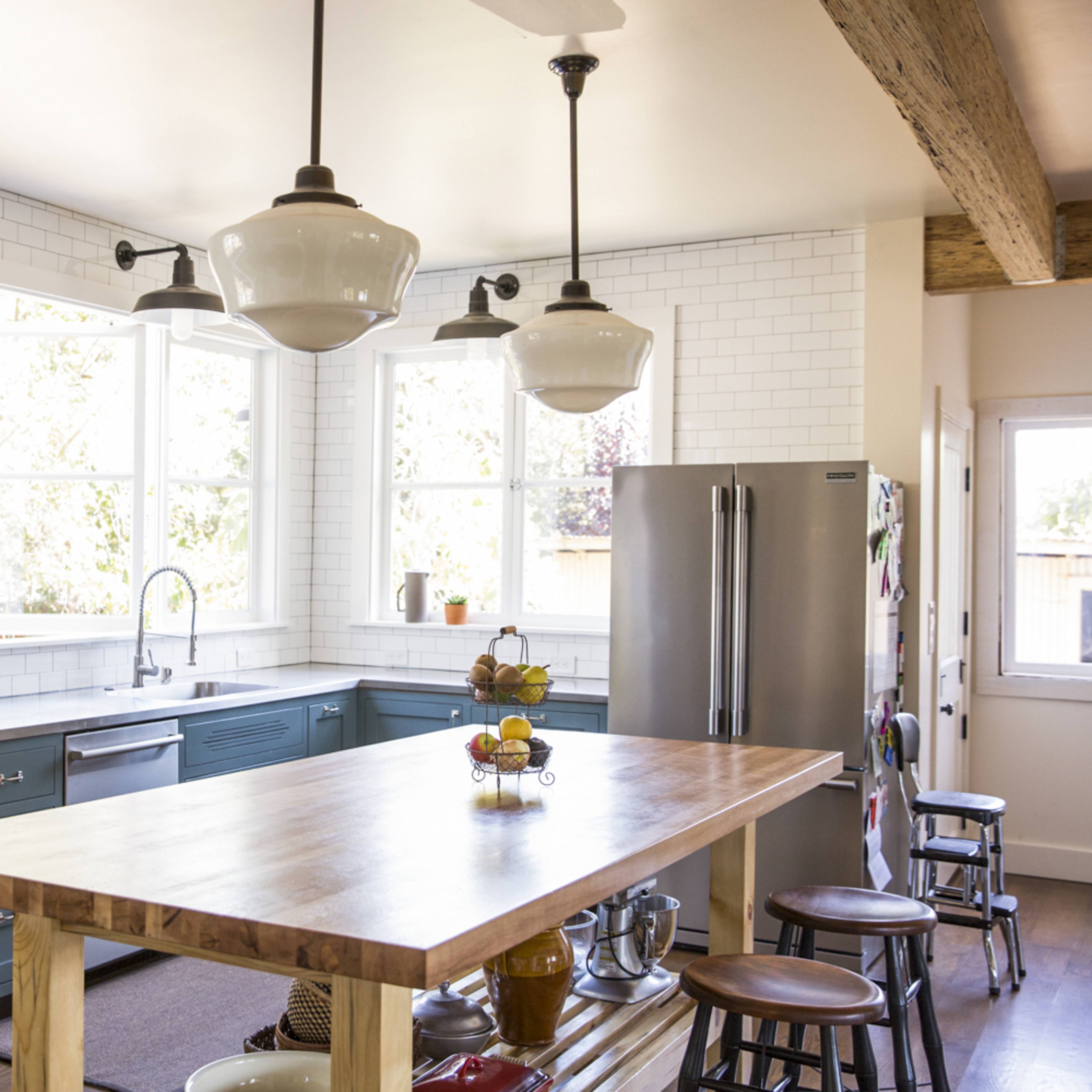 A modern kitchen features a large wooden island, stainless steel appliances, and white subway tile walls.