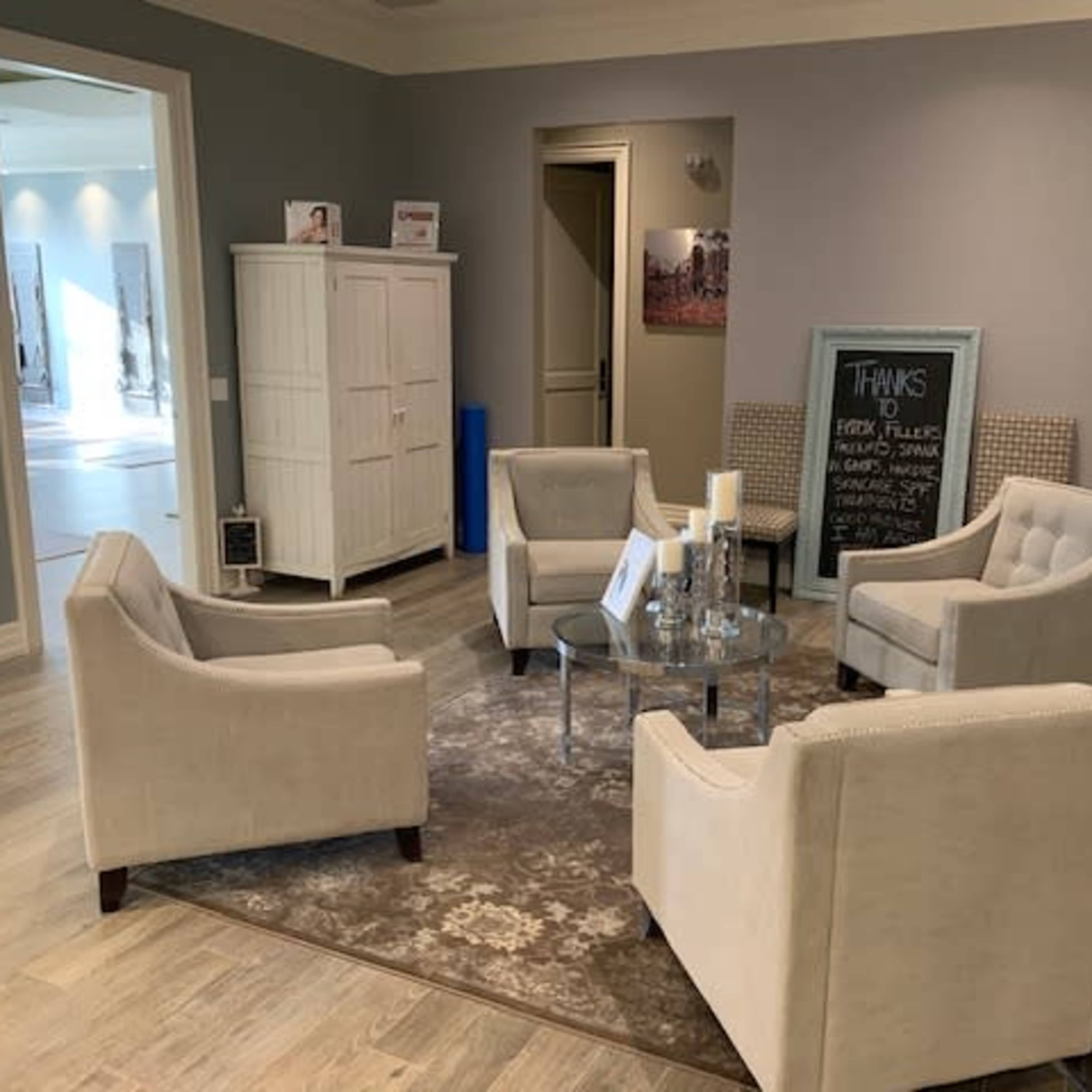 A small waiting area with four upholstered chairs arranged around a glass coffee table on a patterned rug, against a light gray wall.