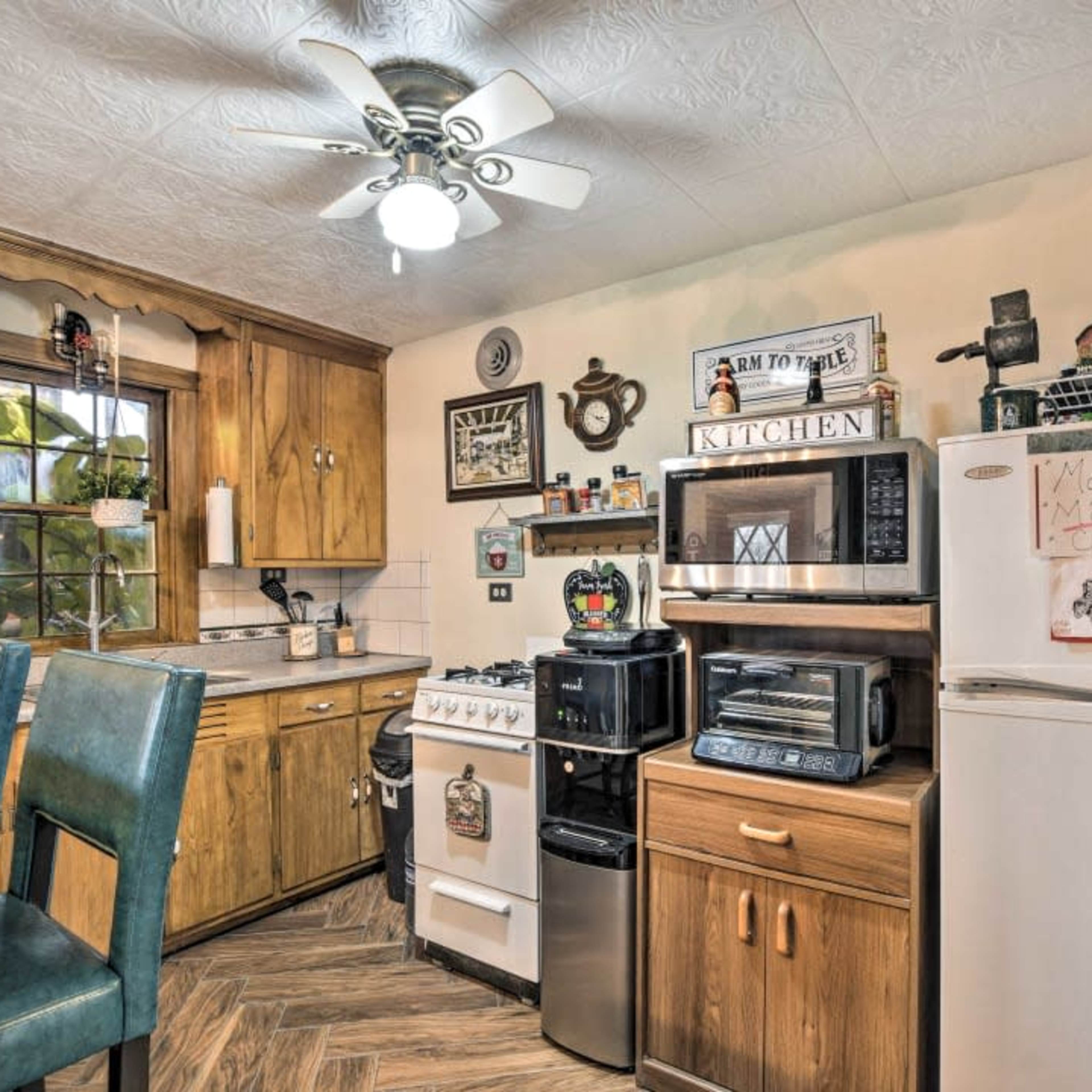 A kitchen with wooden cabinets, a white refrigerator, various appliances, and a dining counter with two blue chairs.