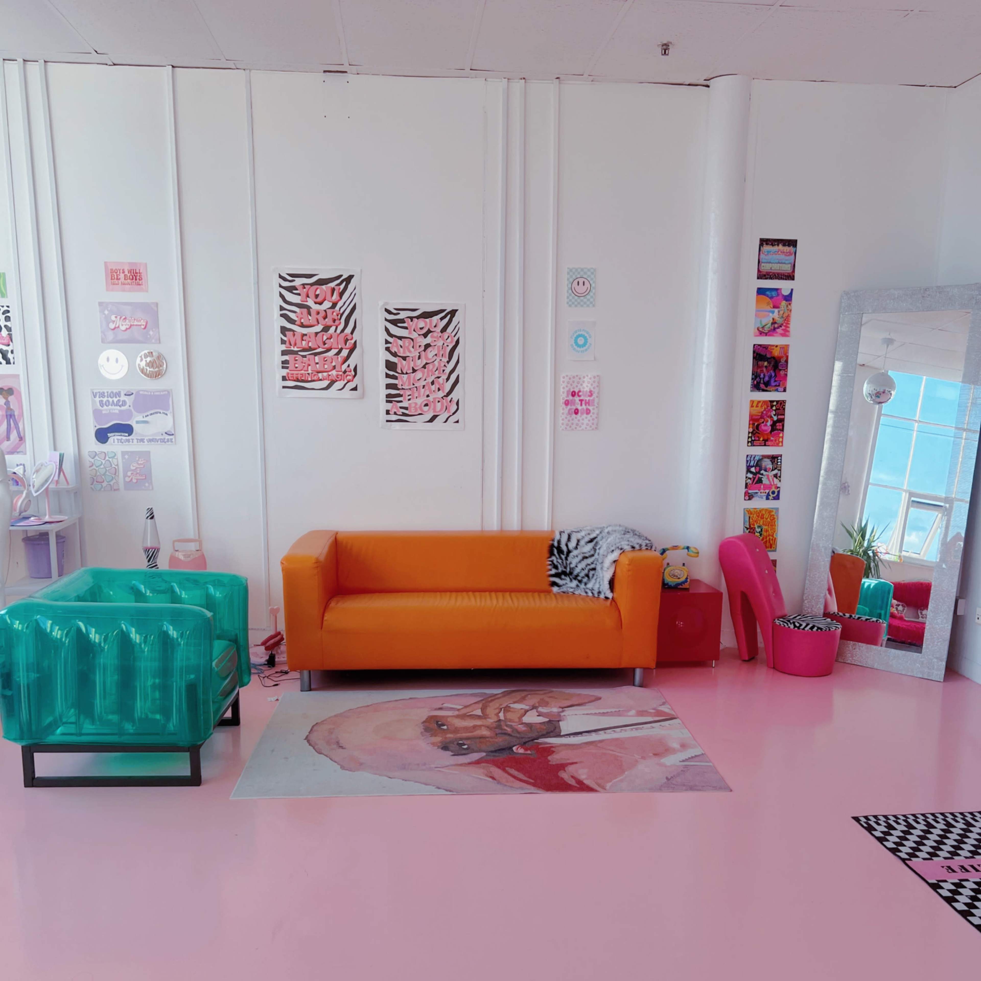 A colorful interior living space featuring an orange sofa, a glass coffee table, a large mirror, and various decorative wall art.